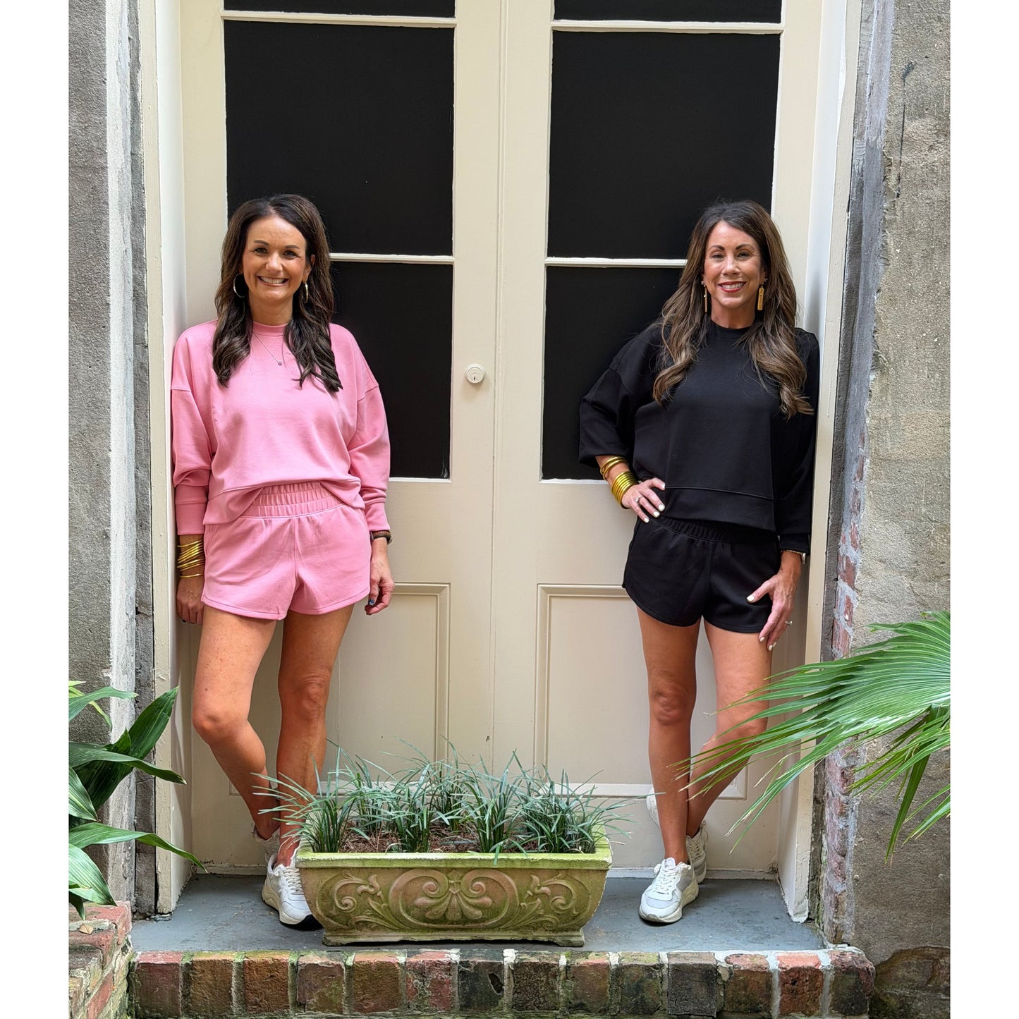 Two women standing in front of a door with plants around.