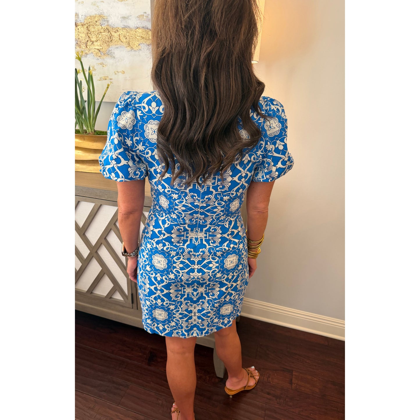 Person wearing a blue floral dress standing in a room with wooden flooring and decorative elements.