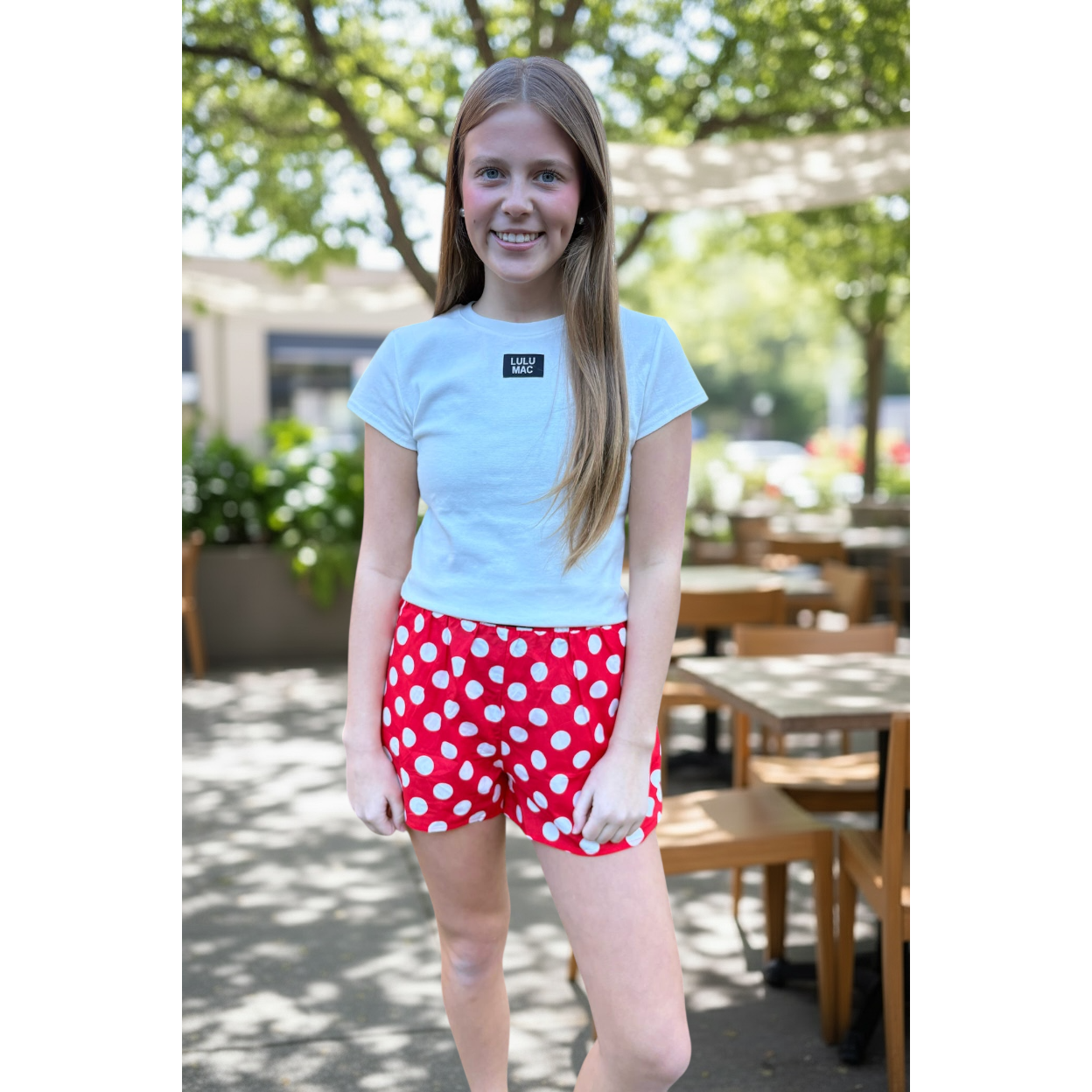 Young girl wearing a light blue t-shirt and red polka dot shorts standing outdoors.