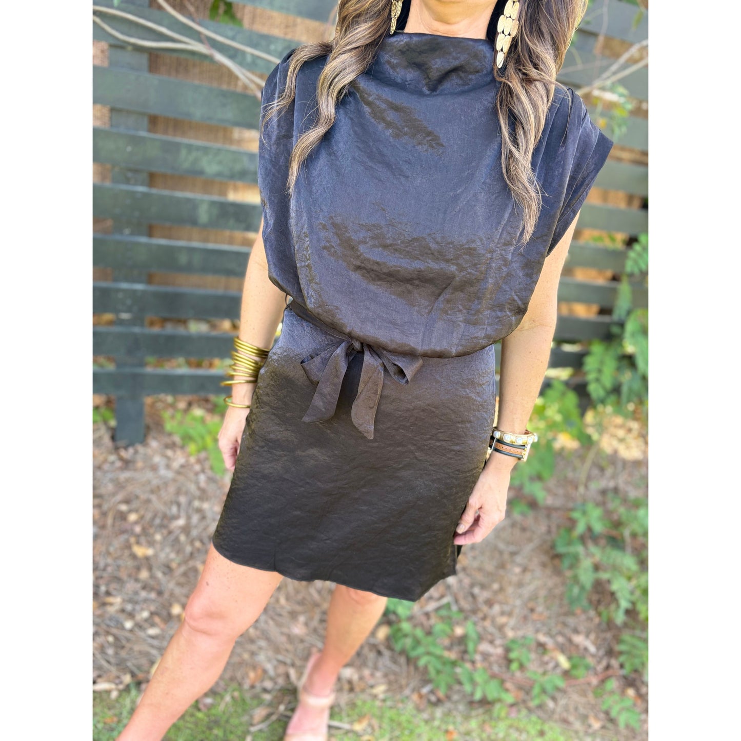 Woman wearing a black dress with a tie detail in an outdoor setting