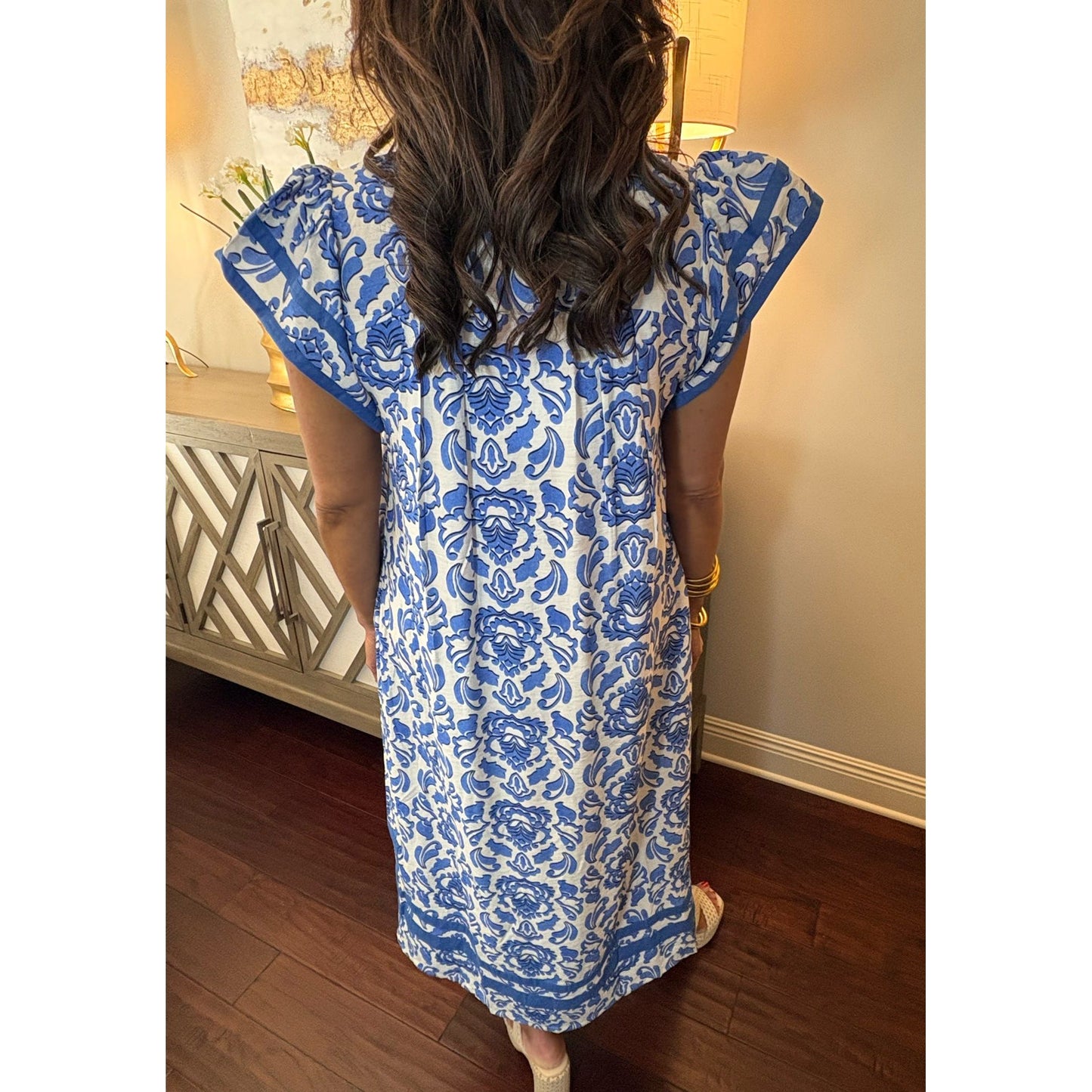 Person wearing a blue and white floral dress standing indoors.