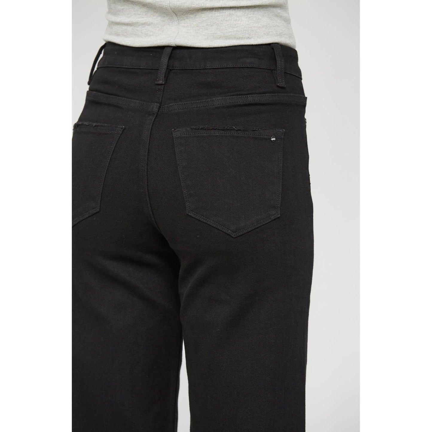 Rear view of a person wearing black denim jeans with a light gray top, cropped from the waist down against a plain light gray background.