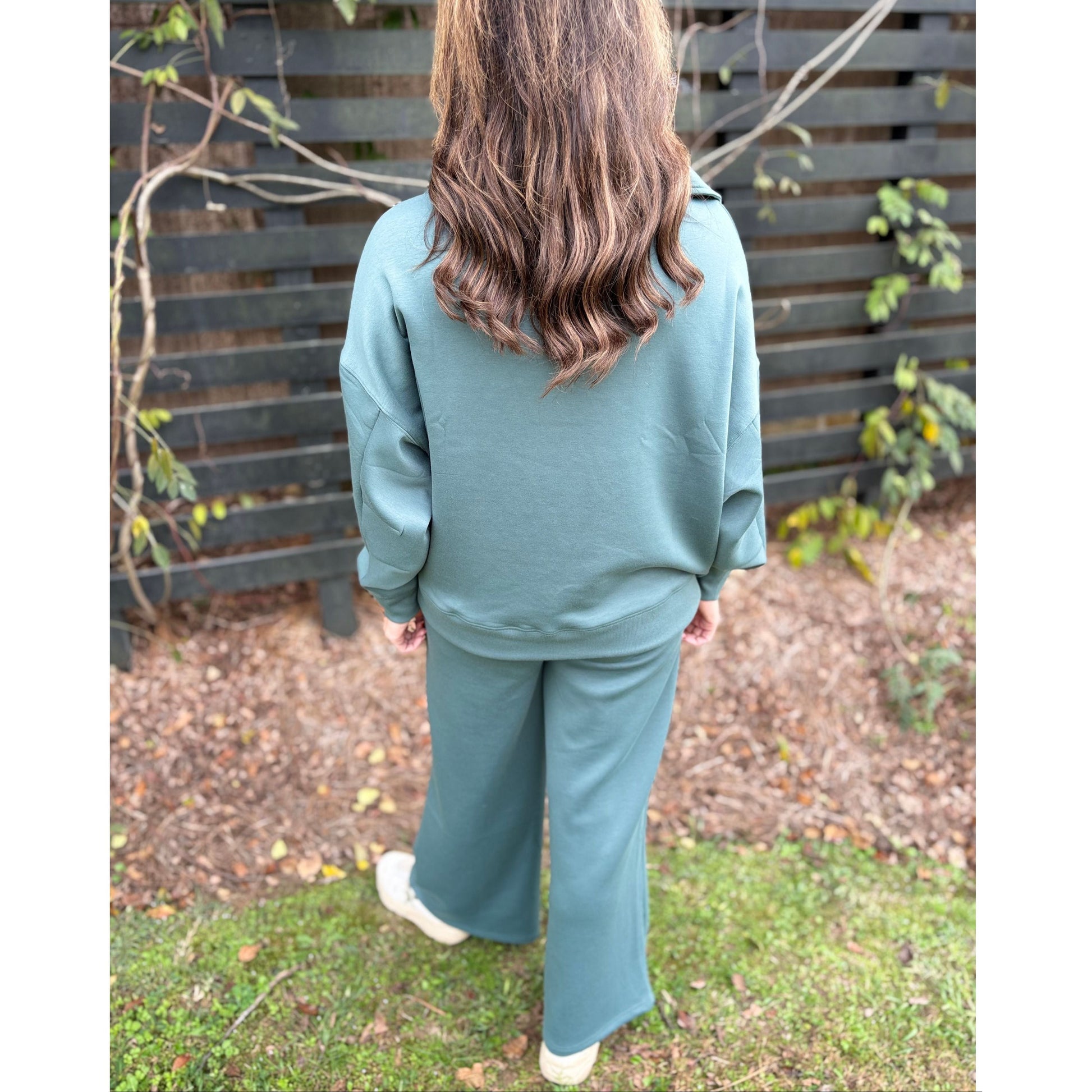 Person wearing a teal tracksuit standing outdoors with a wooden fence and grass in the background