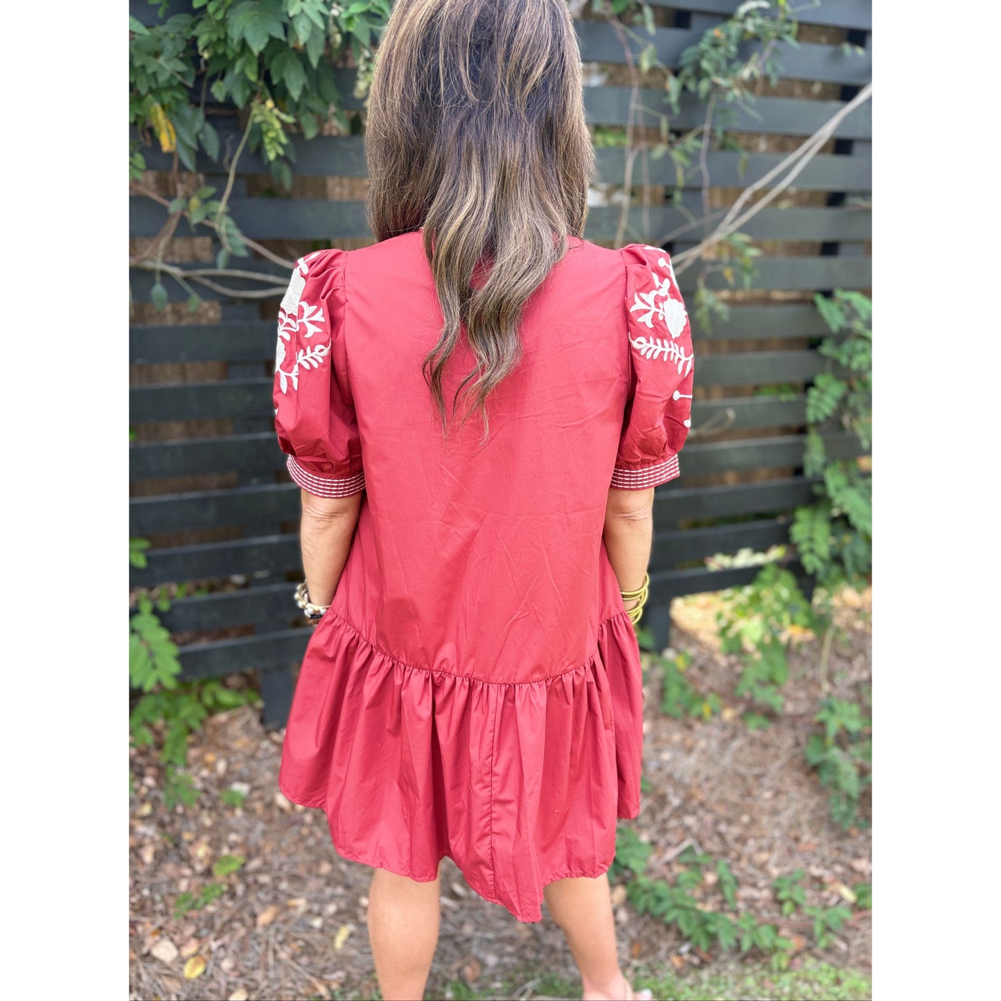Person wearing a red dress with white embroidery standing outdoors.