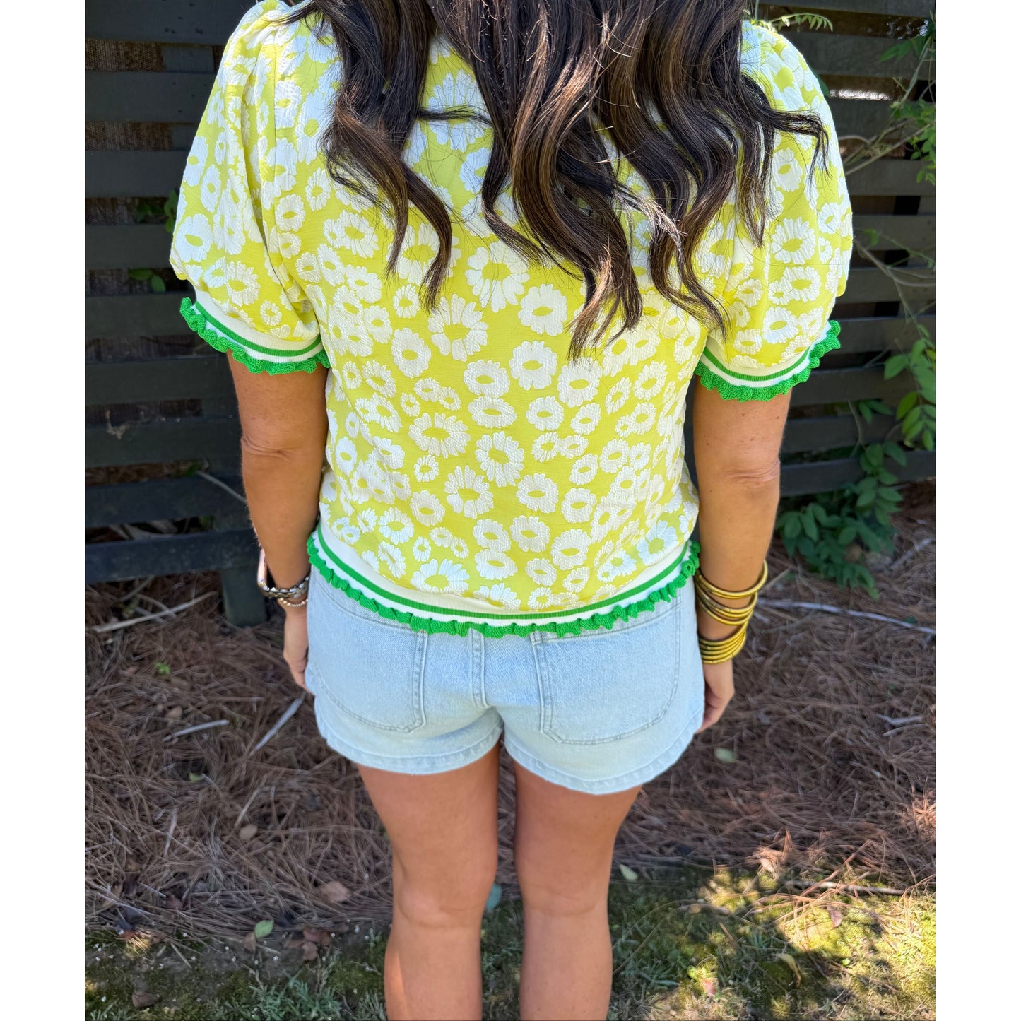 Person wearing a yellow and white patterned dress with green trim outdoors.
