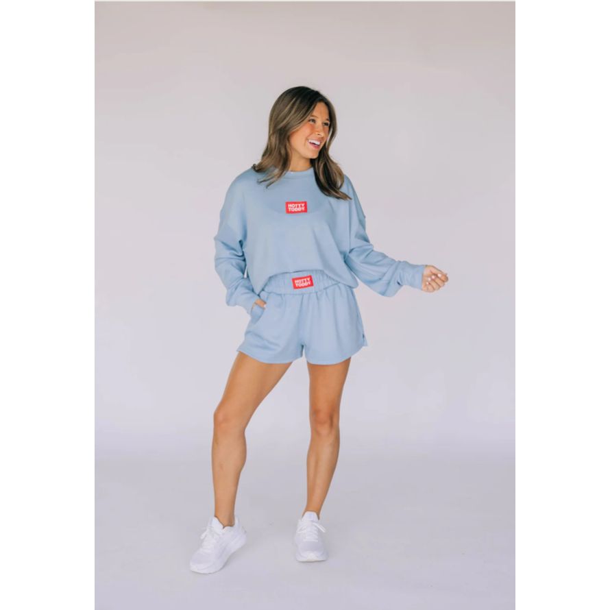 Woman wearing a light blue sweatshirt and shorts set with red labels on a plain background