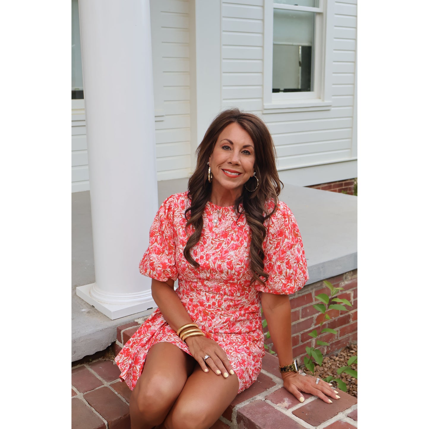 Woman in a red floral dress standing on a brick step with a white building in the background