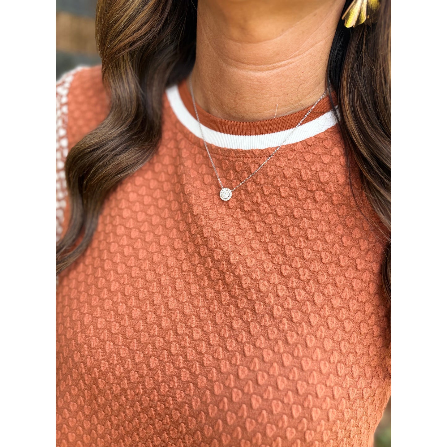 Person wearing a patterned brown top with a necklace