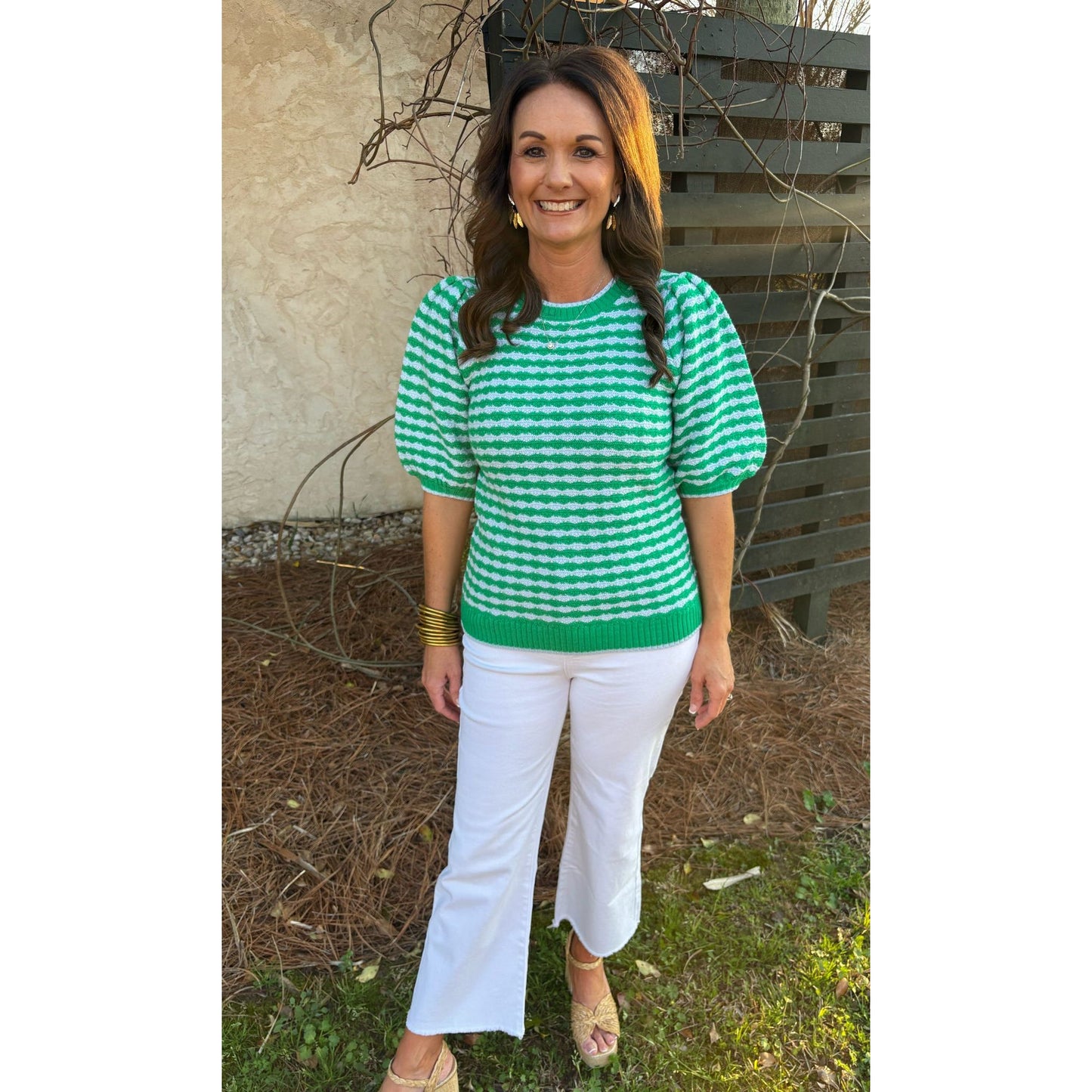 Woman wearing a green and white checkered shirt and white pants standing outdoors.