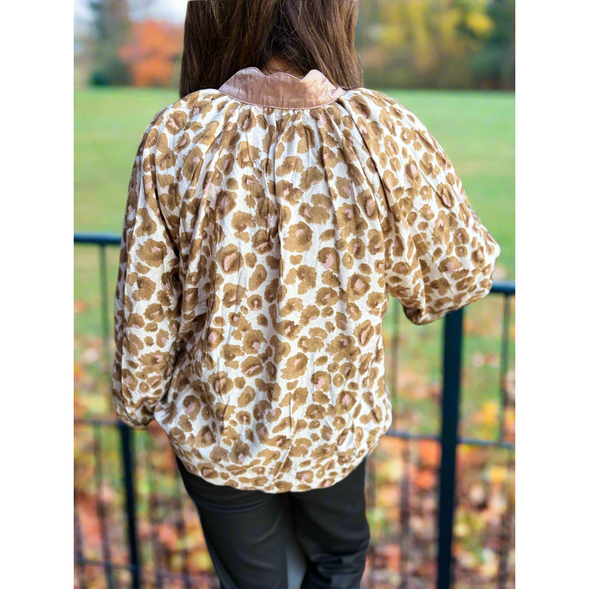 Person wearing a leopard print blouse with a blurred outdoor background