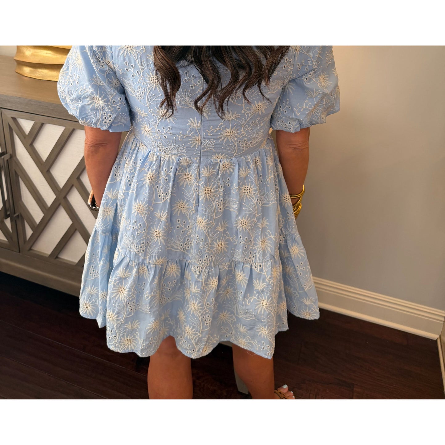 Person wearing a light blue dress with floral patterns indoors.