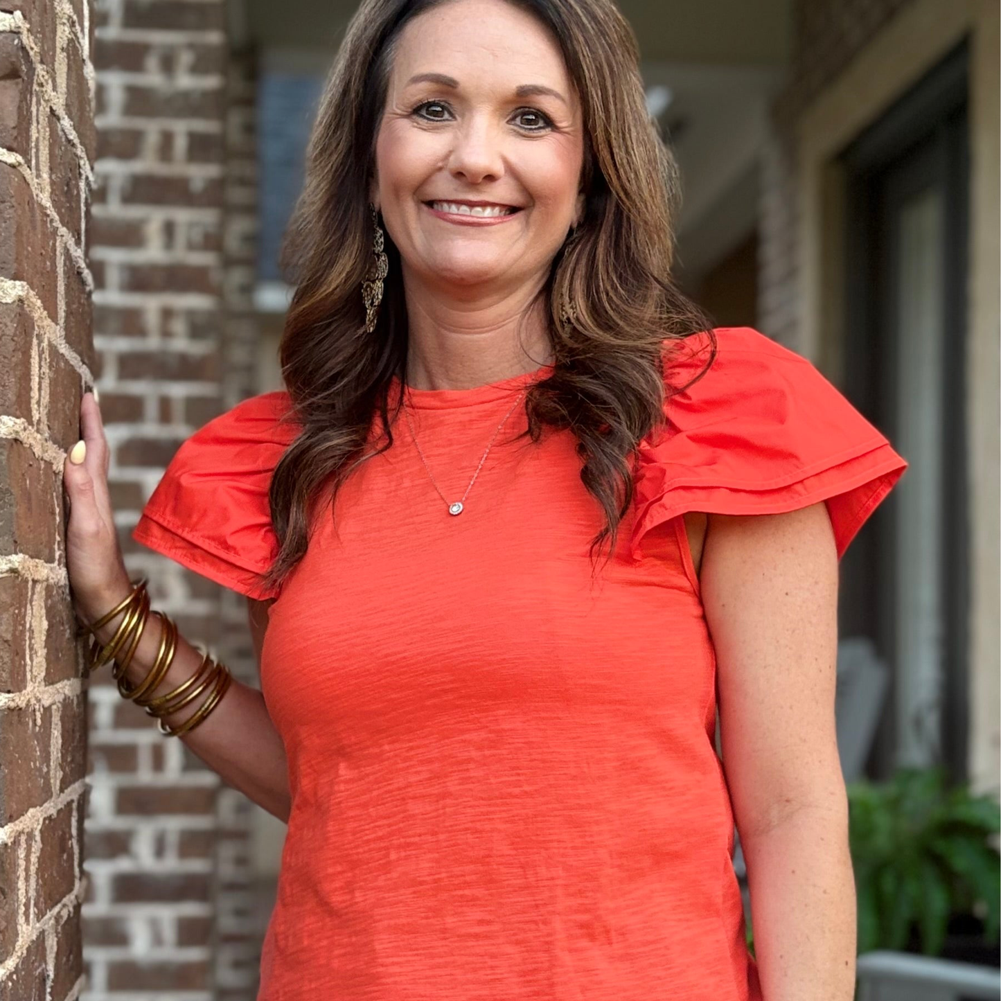 Woman in a red dress standing against a brick wall