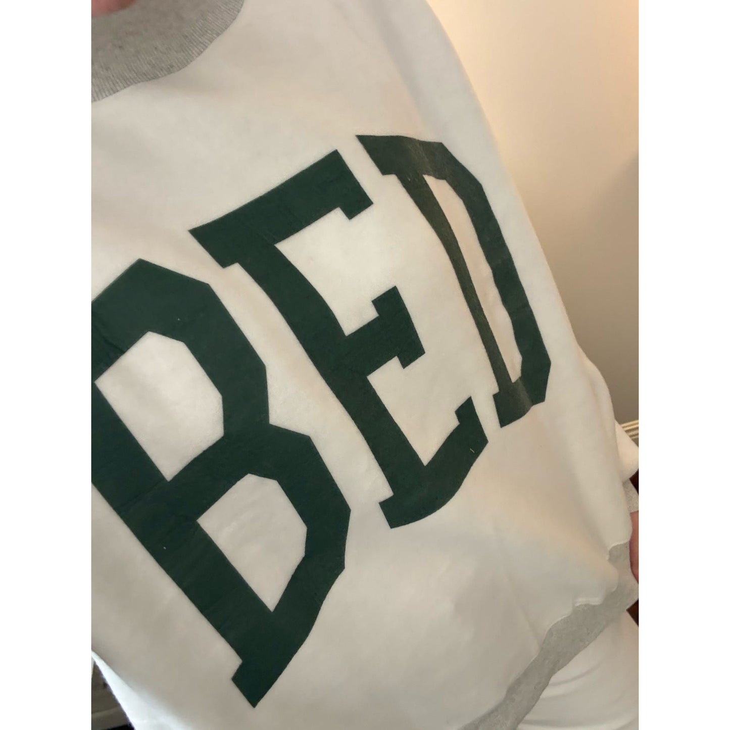 White garment with green letters spelling 'BED' held by a person.