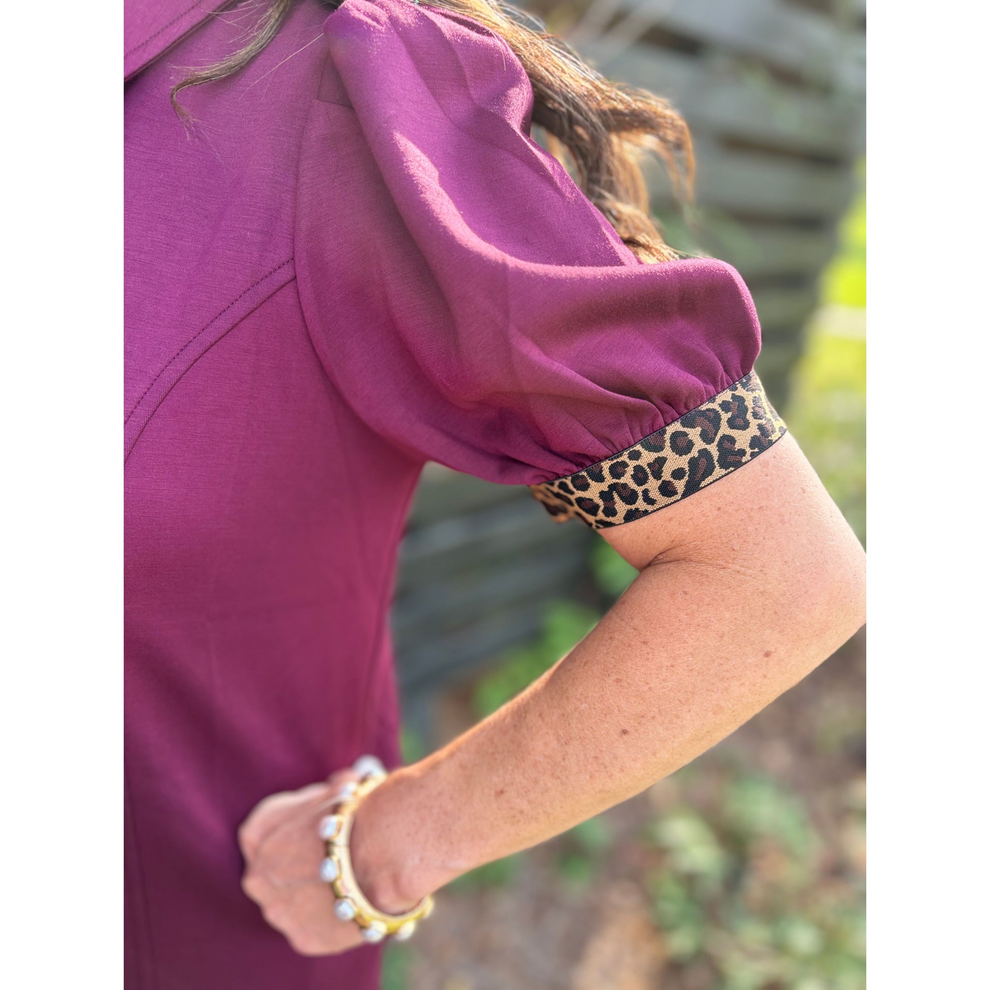 Person wearing a purple shirt with a leopard print arm band and bracelets.