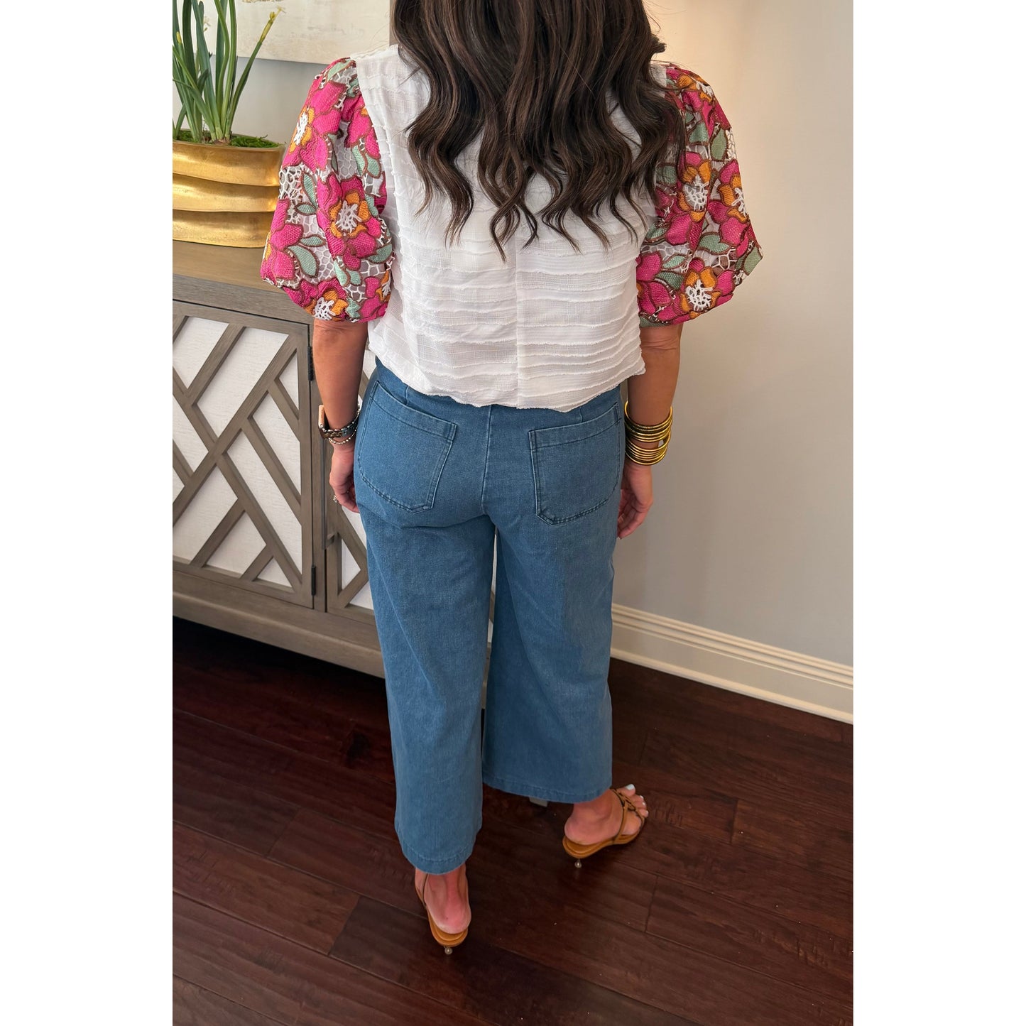 Woman wearing a floral blouse and blue jeans in an indoor setting.