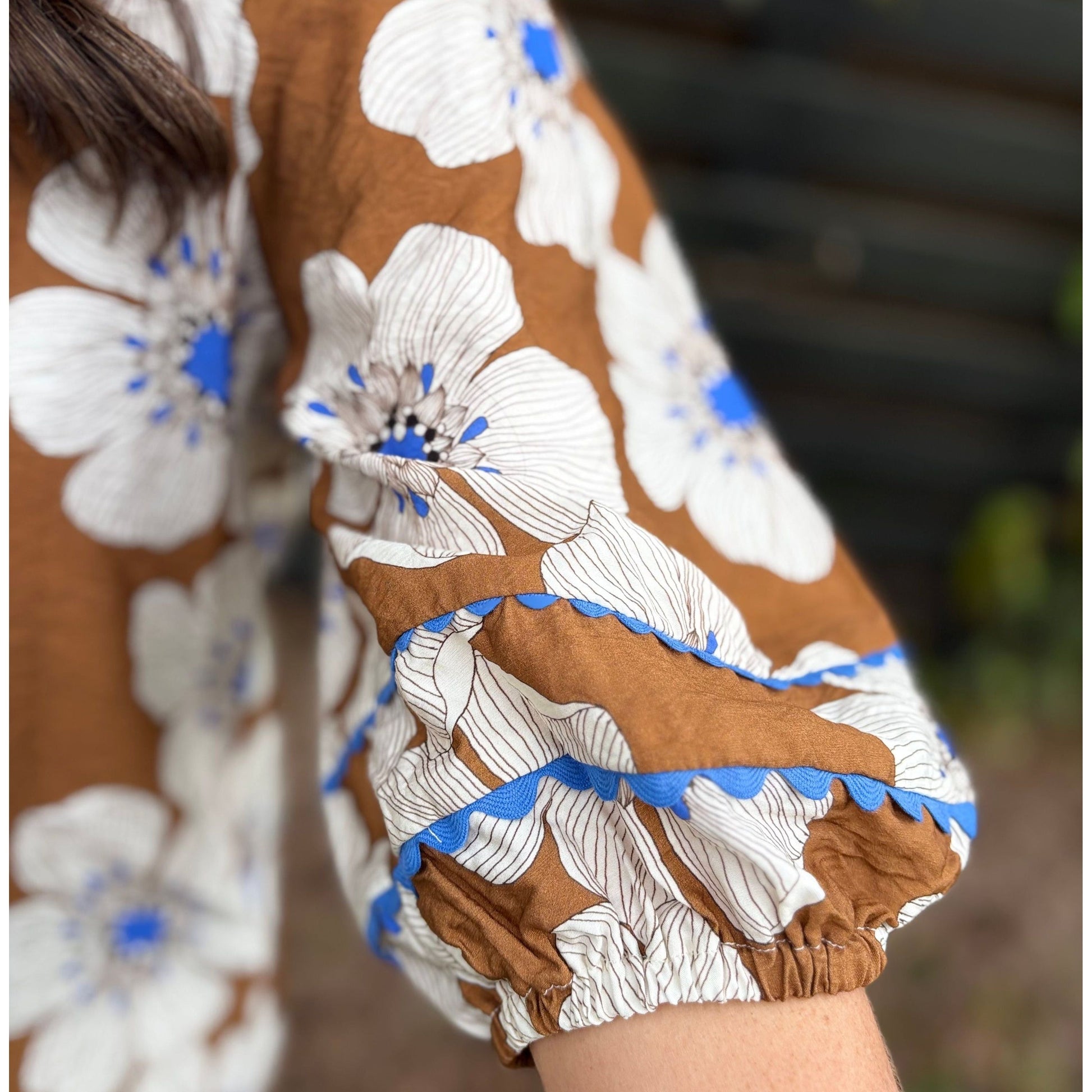 Close-up of a person wearing a brown floral dress with white flowers and blue accents.