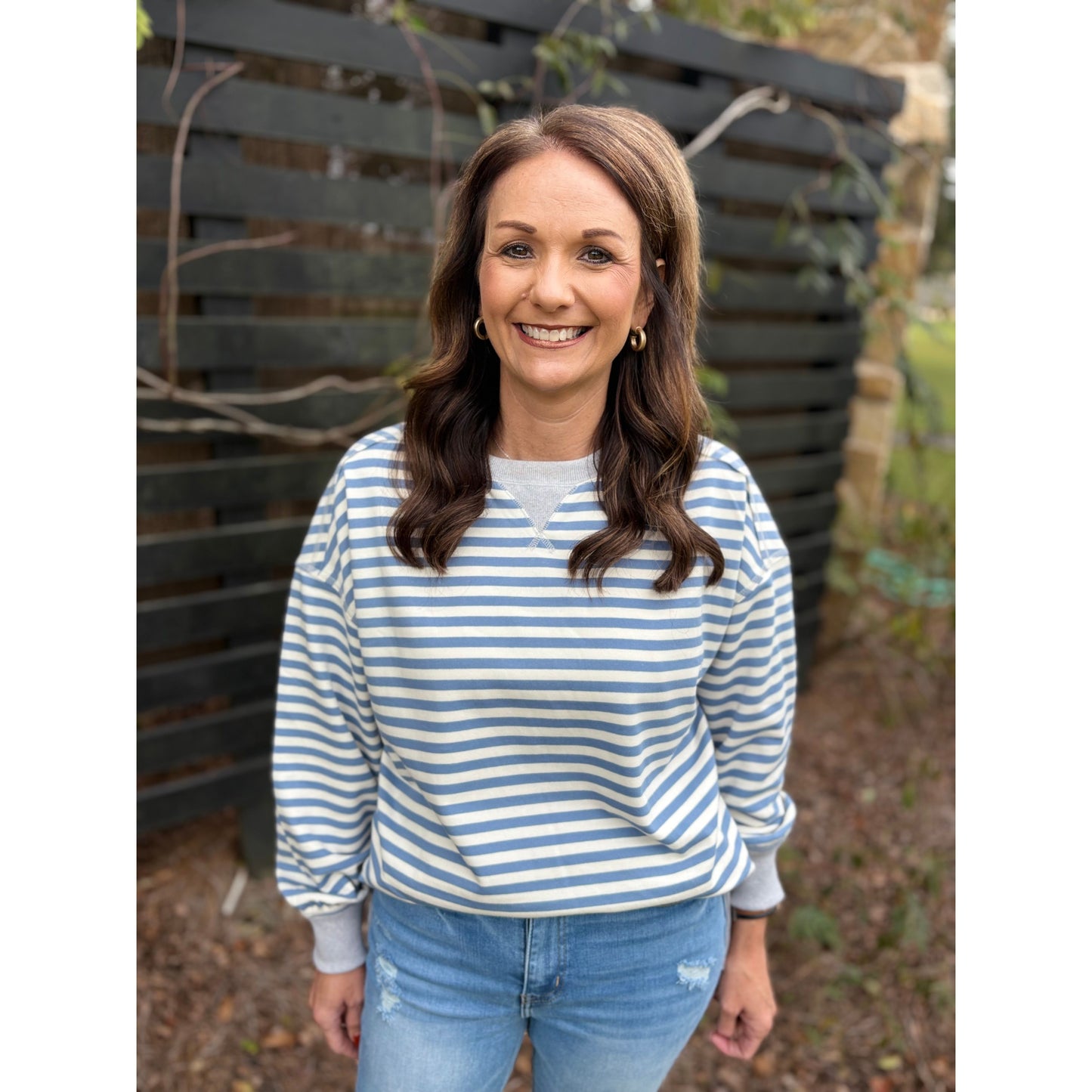 Woman wearing a blue and white striped shirt and jeans standing in front of a wooden fence.