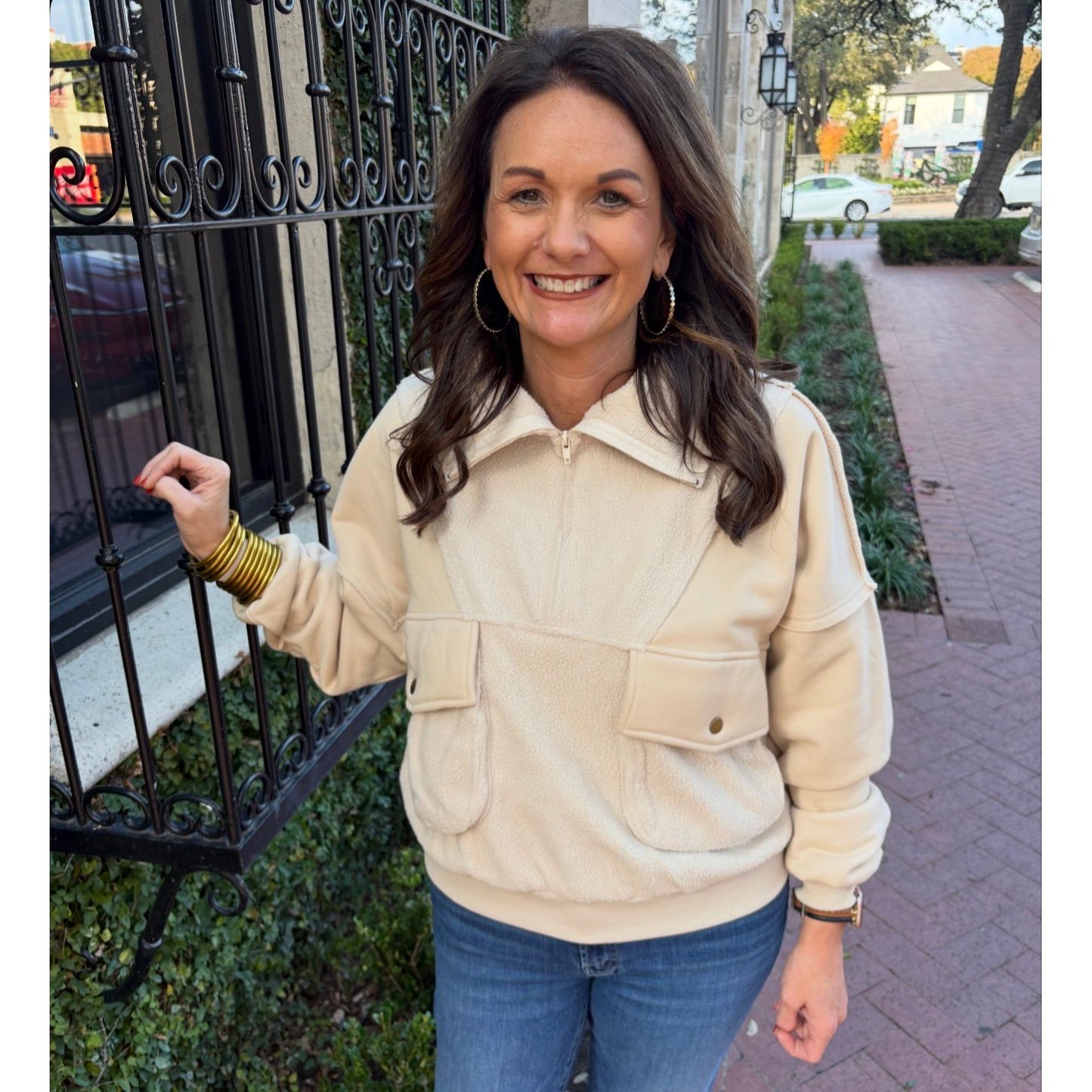 Woman wearing a beige jacket and blue jeans standing on a sidewalk.