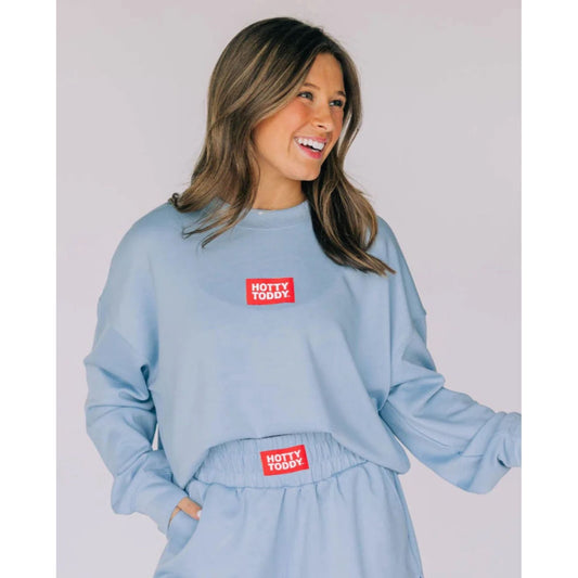 Woman wearing a light blue sweatshirt and pants with 'Hotty Toddy' logo on a plain background