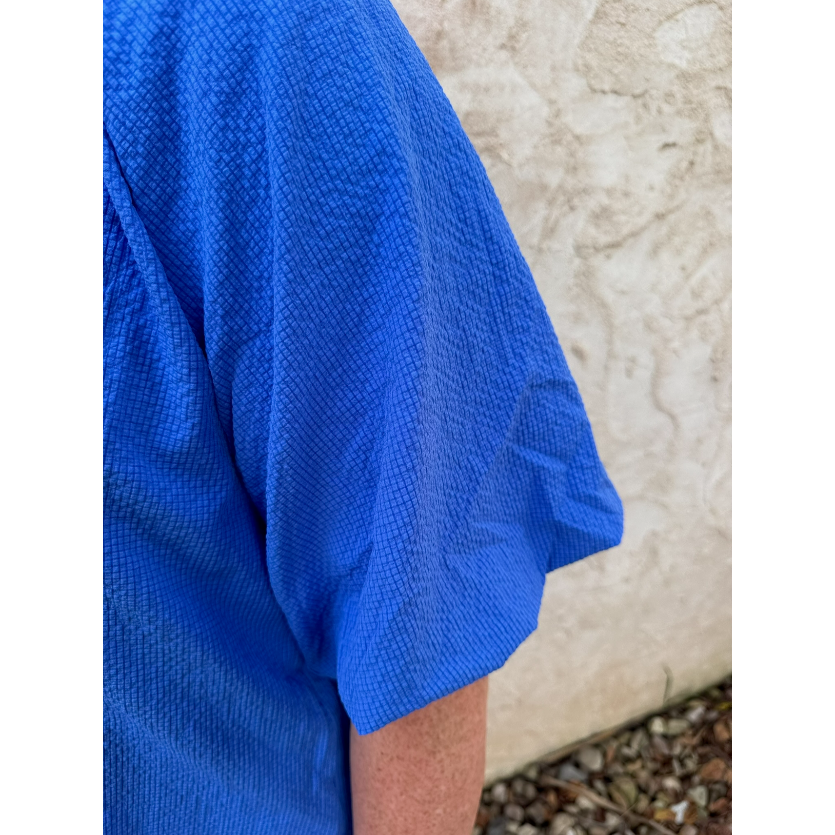 Blue shirt worn by a person against a stone wall background