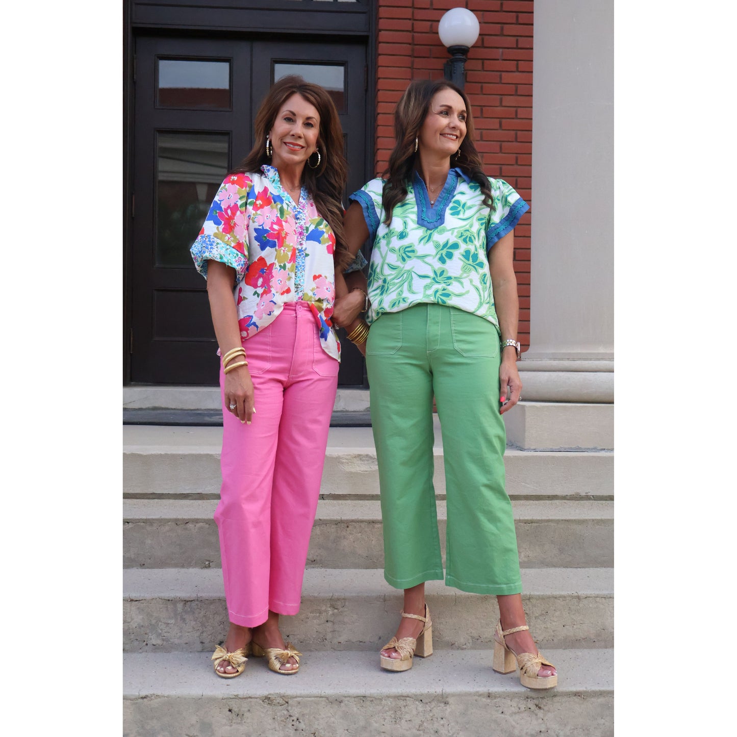 Two women standing on steps wearing colorful outfits with floral tops and bright pants.