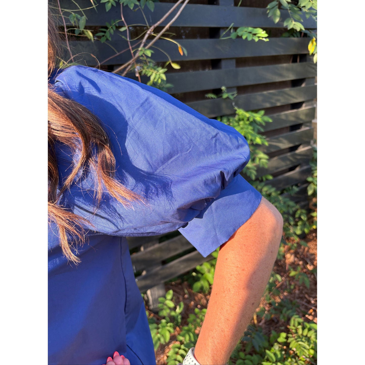 Person wearing a blue raincoat with a background of greenery and a wooden fence.
