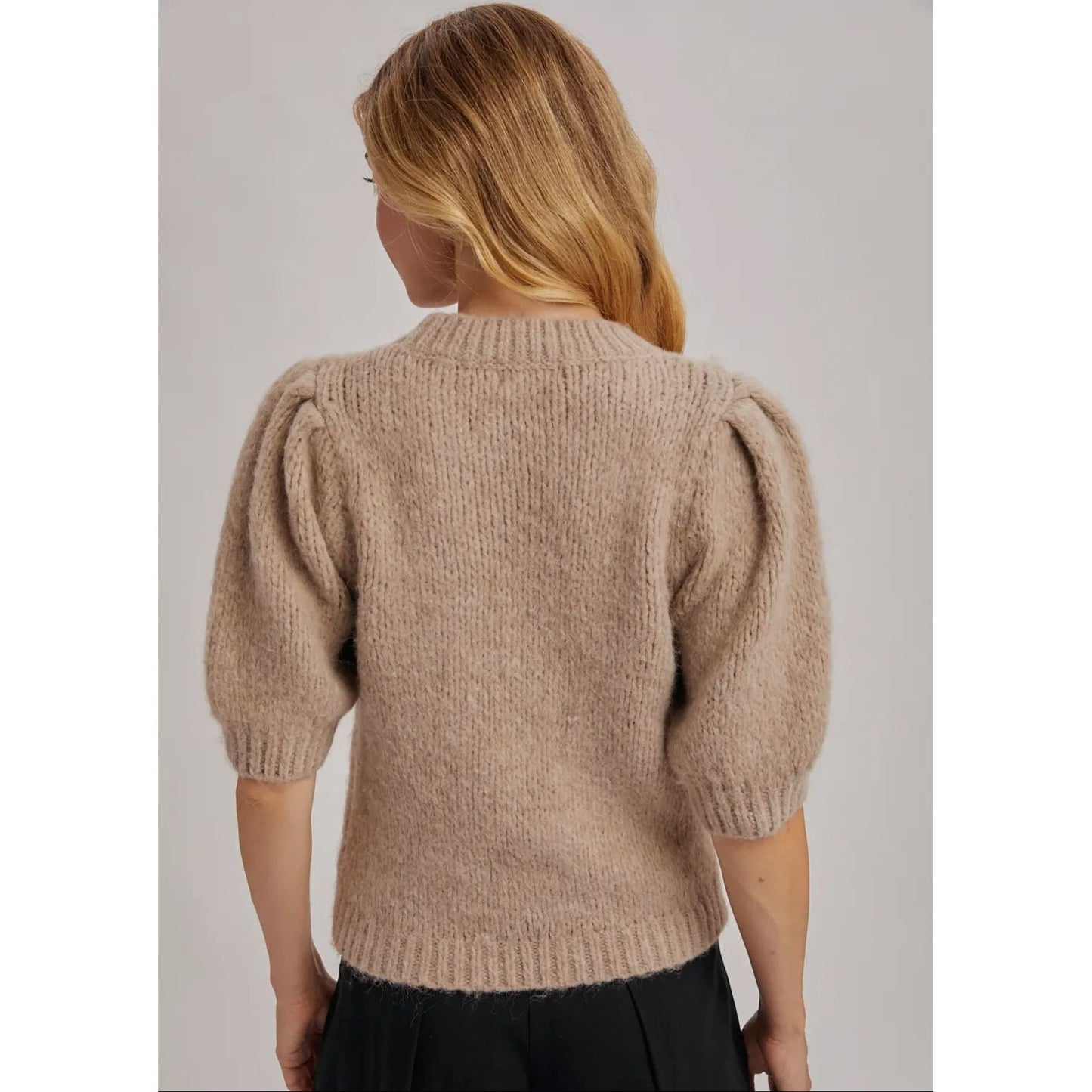 Person wearing a beige knitted sweater with puff sleeves on a plain background
