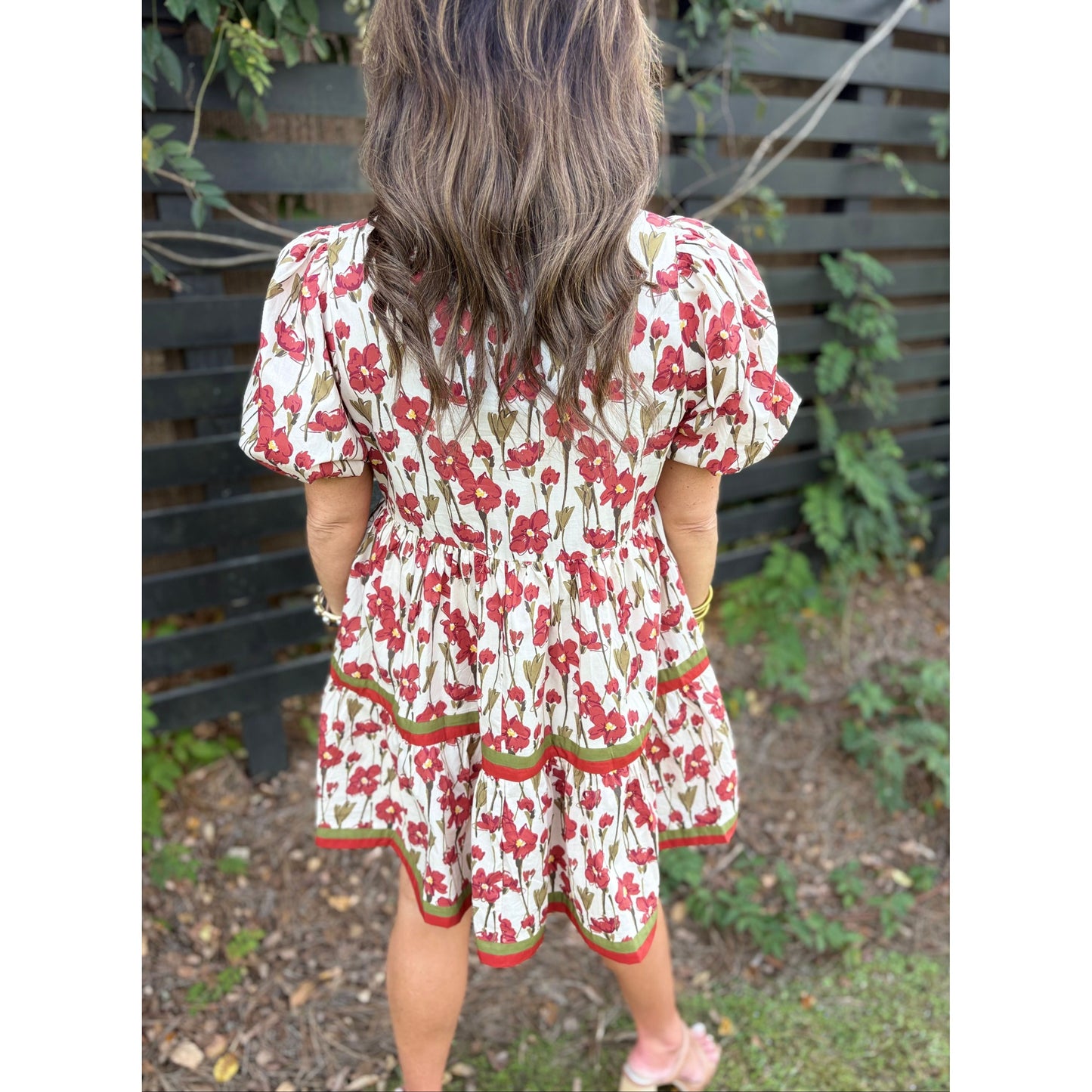 Child wearing a floral dress standing outdoors with greenery in the background