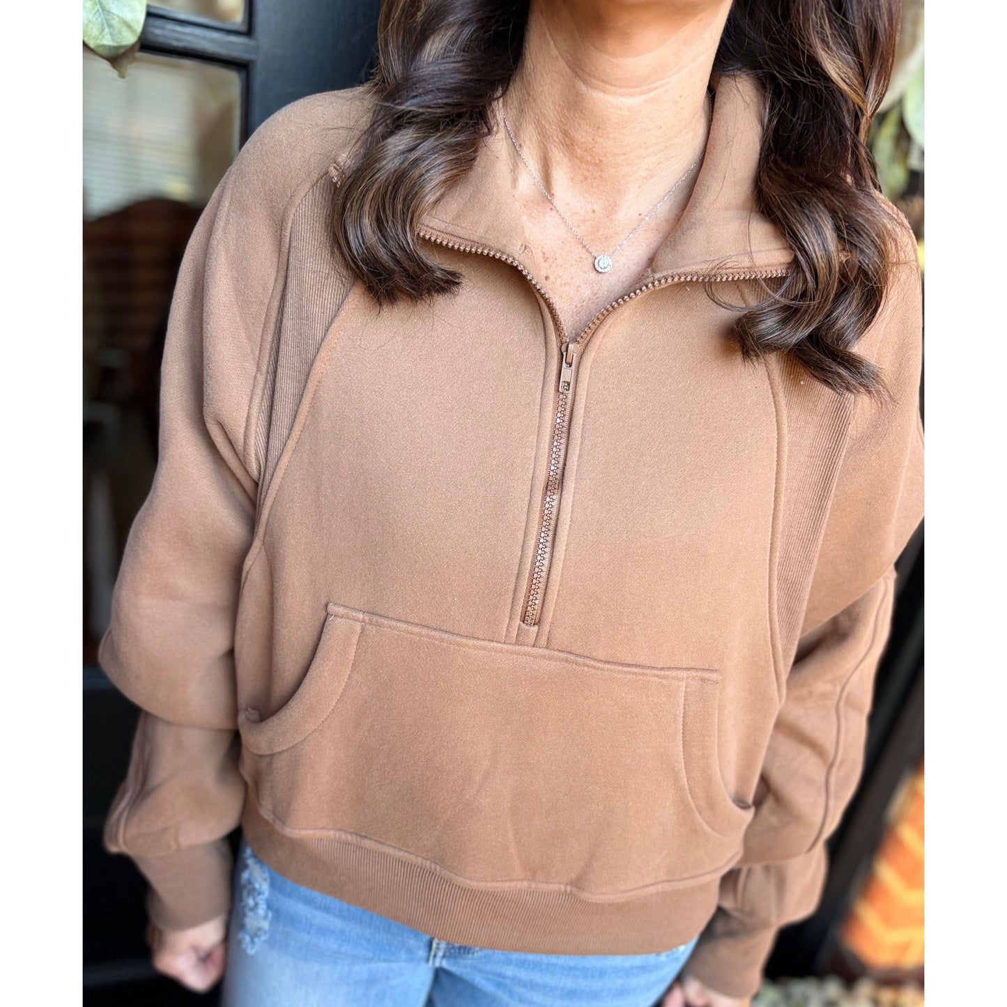 Person wearing a brown half-zip sweatshirt with a blurred background