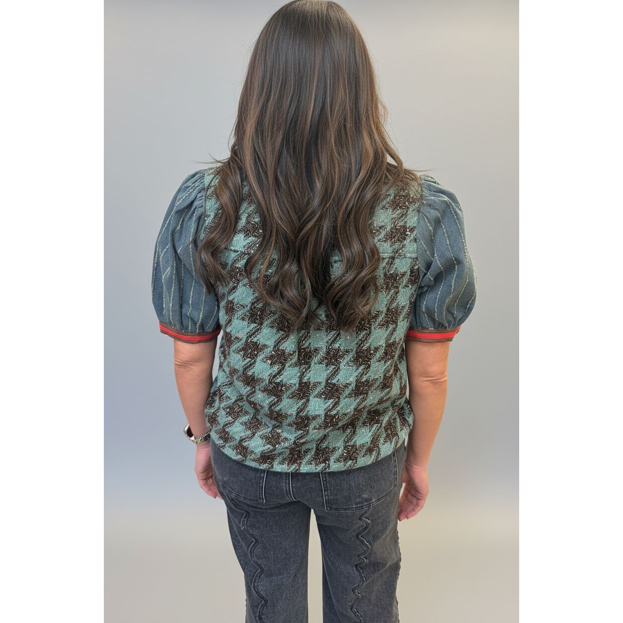 A woman viewed from behind wearing a patterned puff-sleeve top and dark gray jeans in an indoor boutique setting.