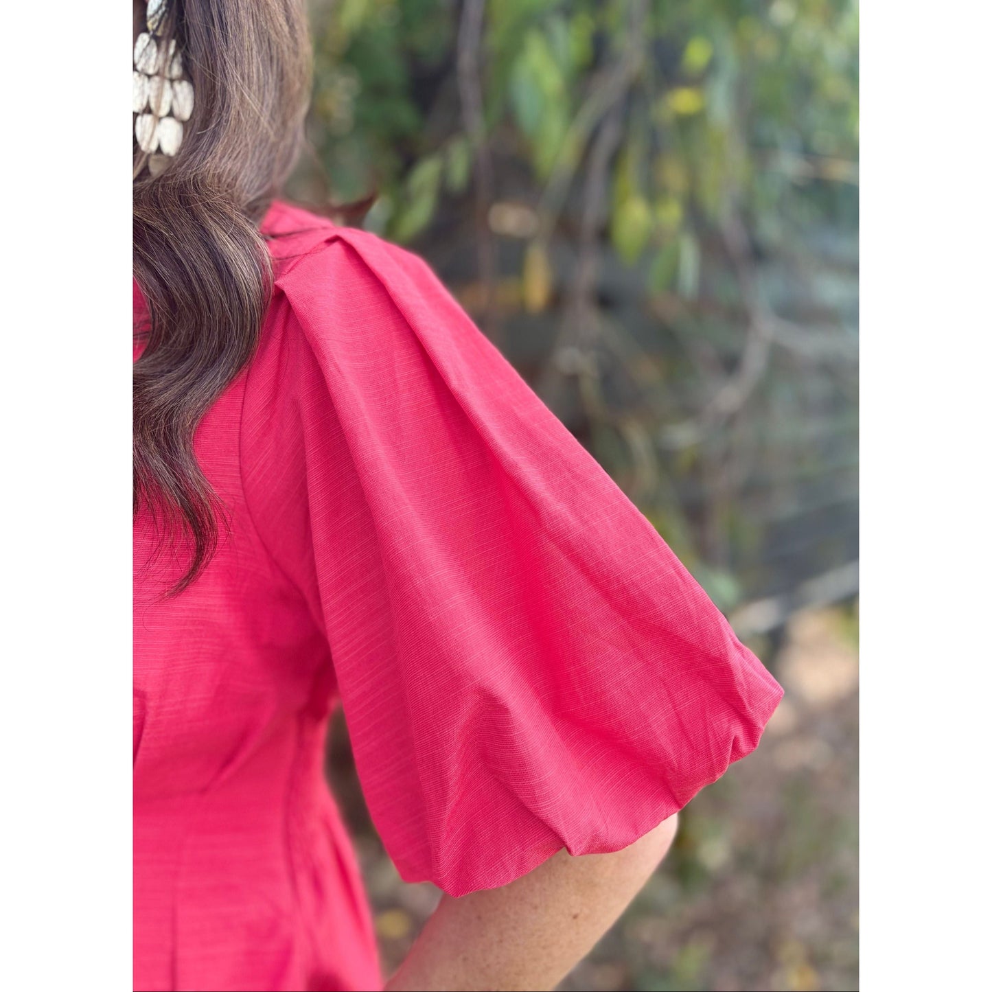Person wearing a pink blouse with short sleeves against a blurred natural background