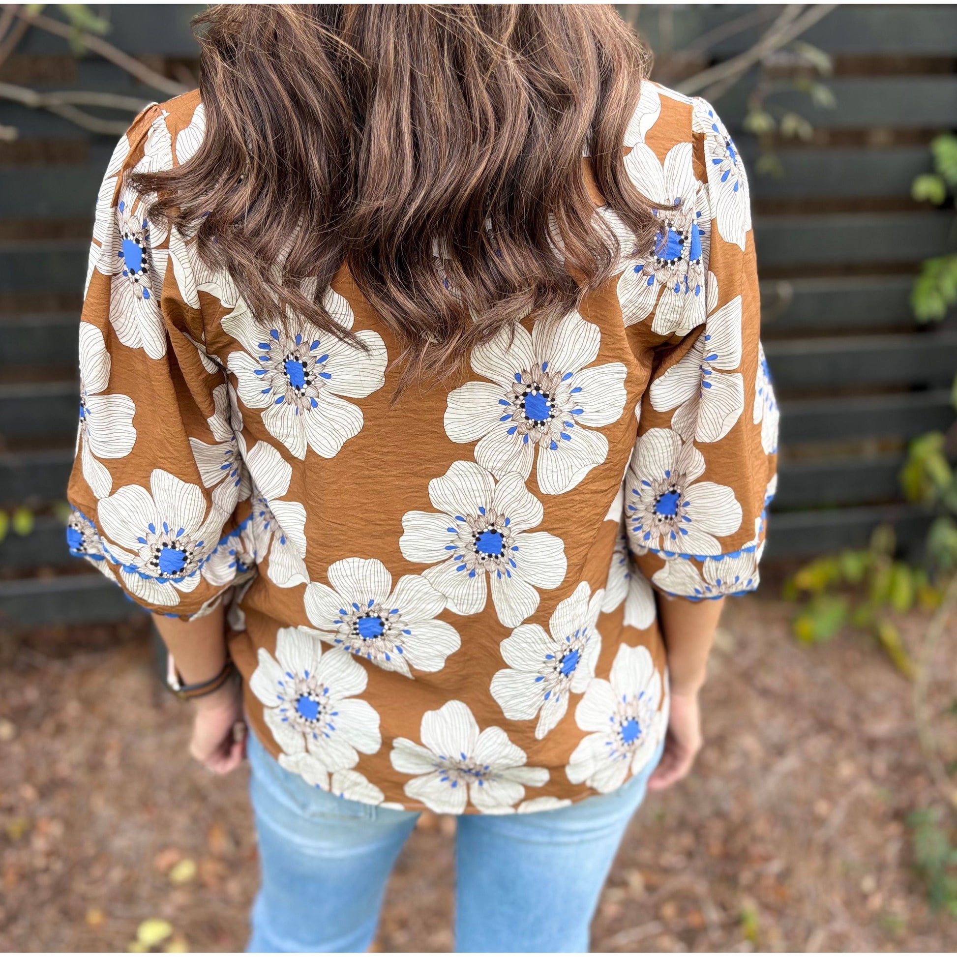 Person wearing a brown floral blouse with blue accents outdoors.