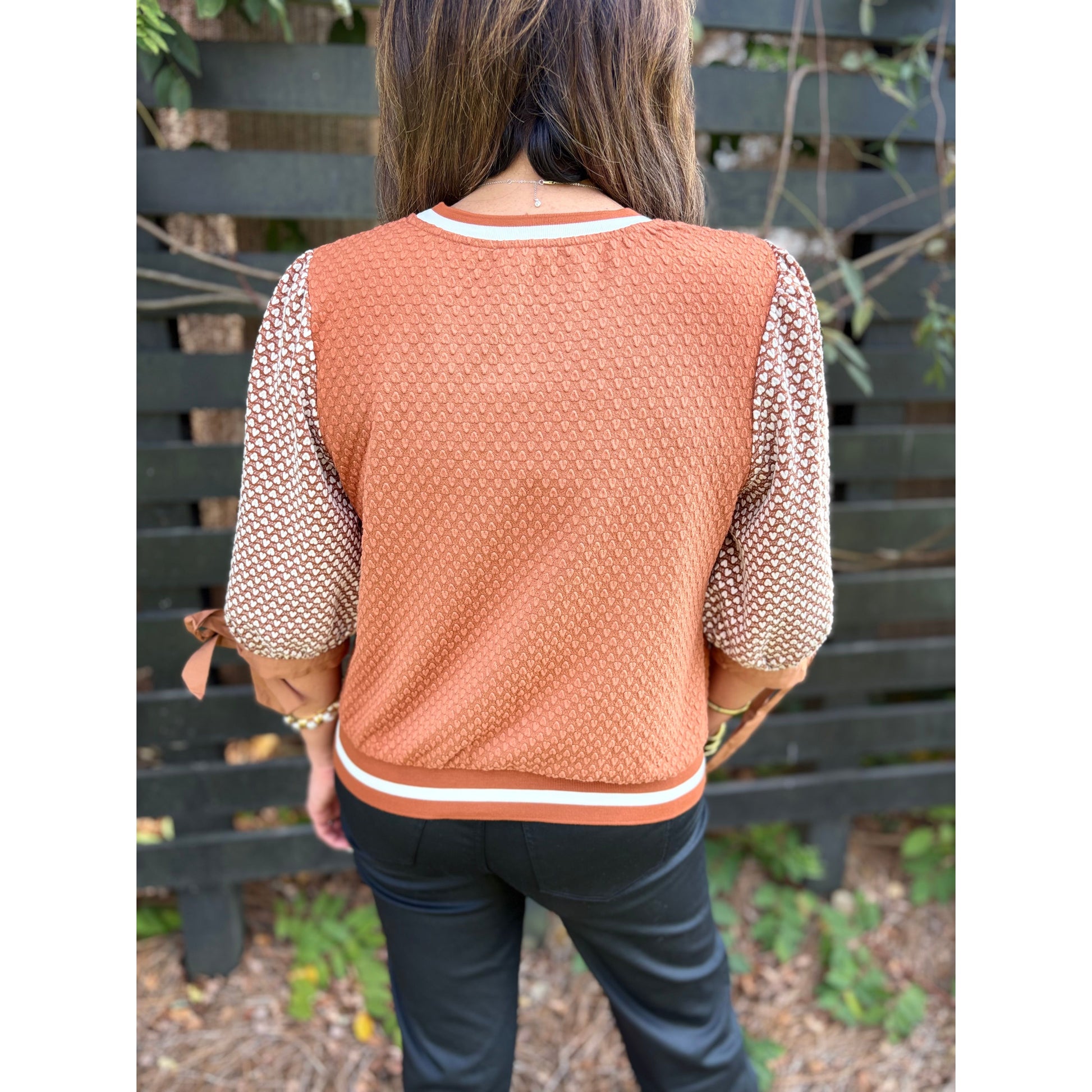 Person wearing a brown textured sweater with patterned sleeves against a wooden fence background