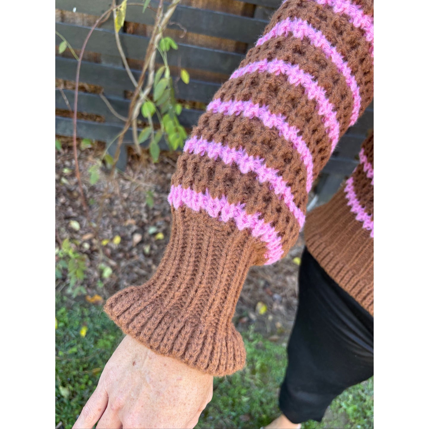 Brown and pink knitted arm warmers worn by a person outdoors.