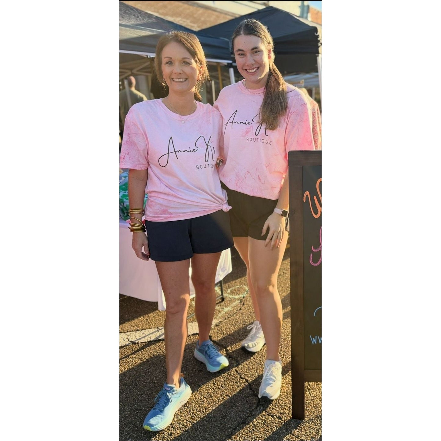 Two women wearing pink t-shirts with a logo, standing outdoors.