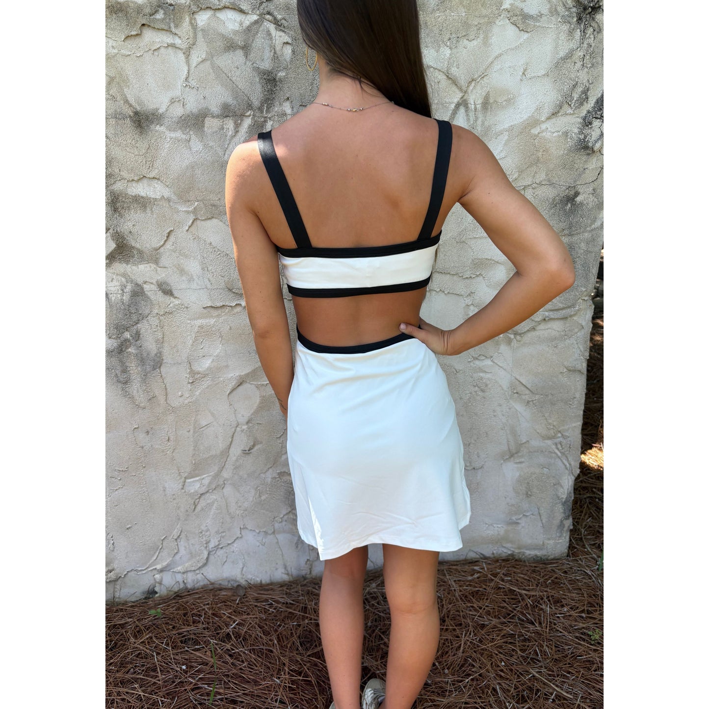 Person wearing a white dress with black straps against a stone wall.