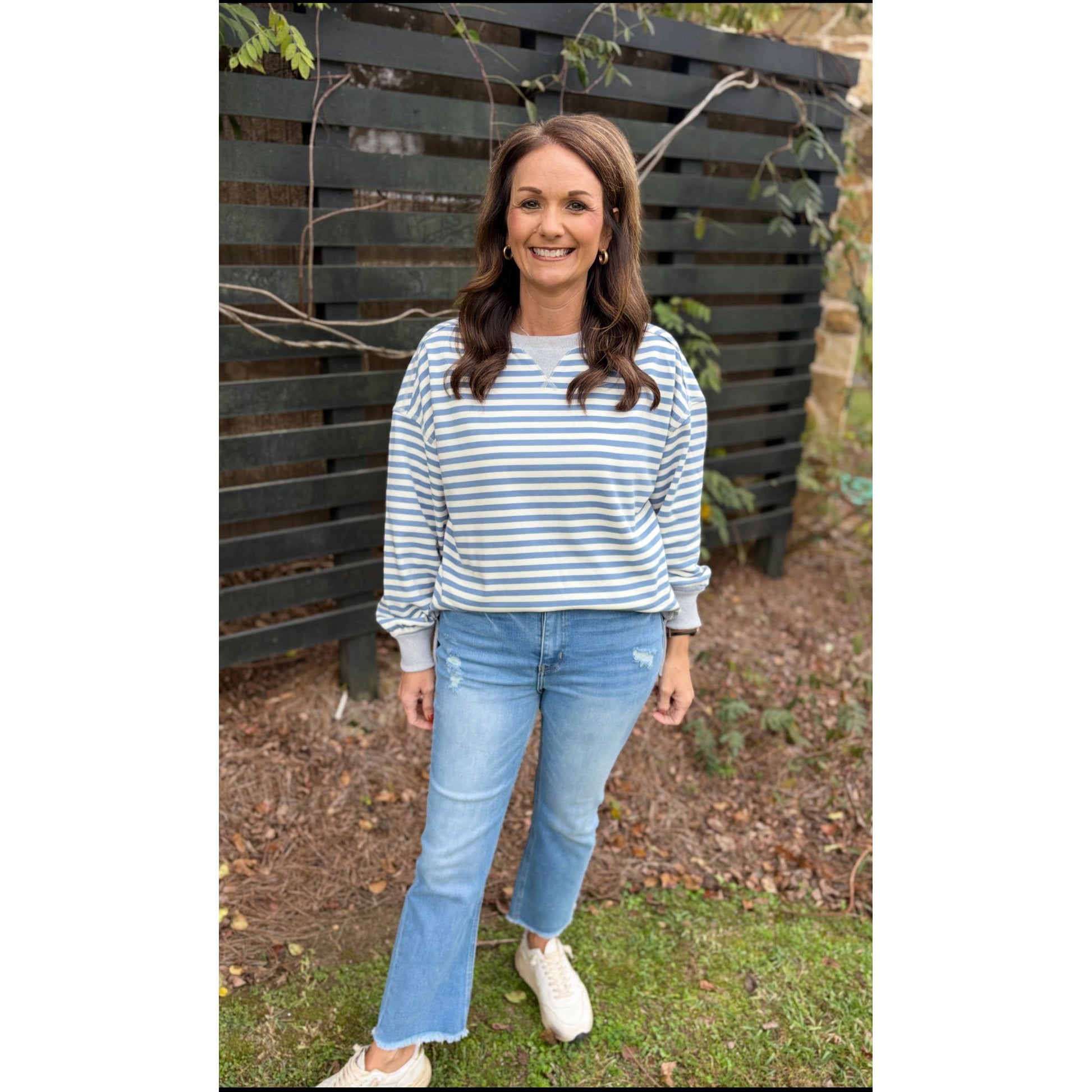 Woman wearing a striped sweater and jeans standing in front of a wooden fence.