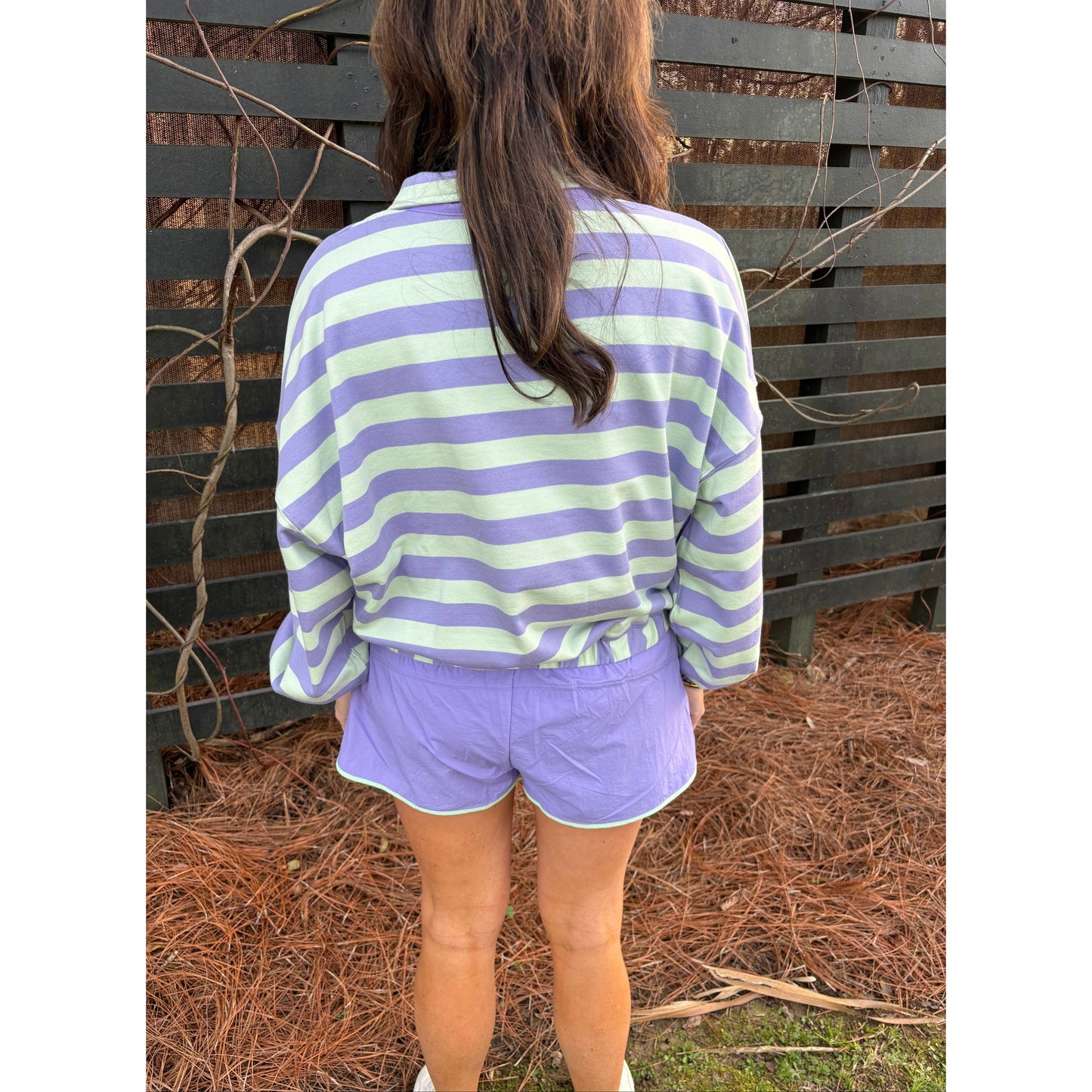 Person wearing a purple and white striped shirt and shorts sitting on a bench with a natural background.