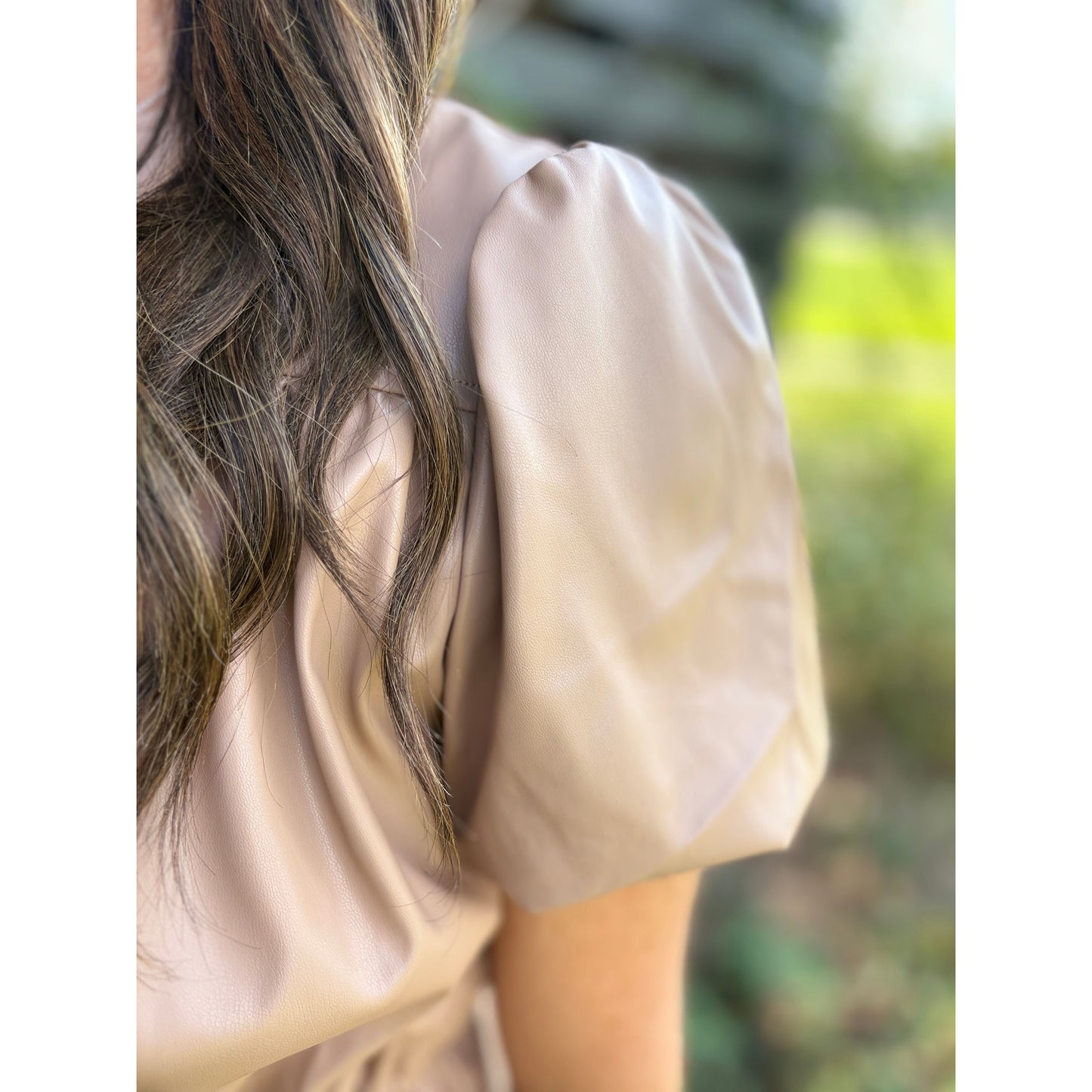 Close-up of a person wearing a light-colored blouse with puffed sleeves against a blurred natural background.
