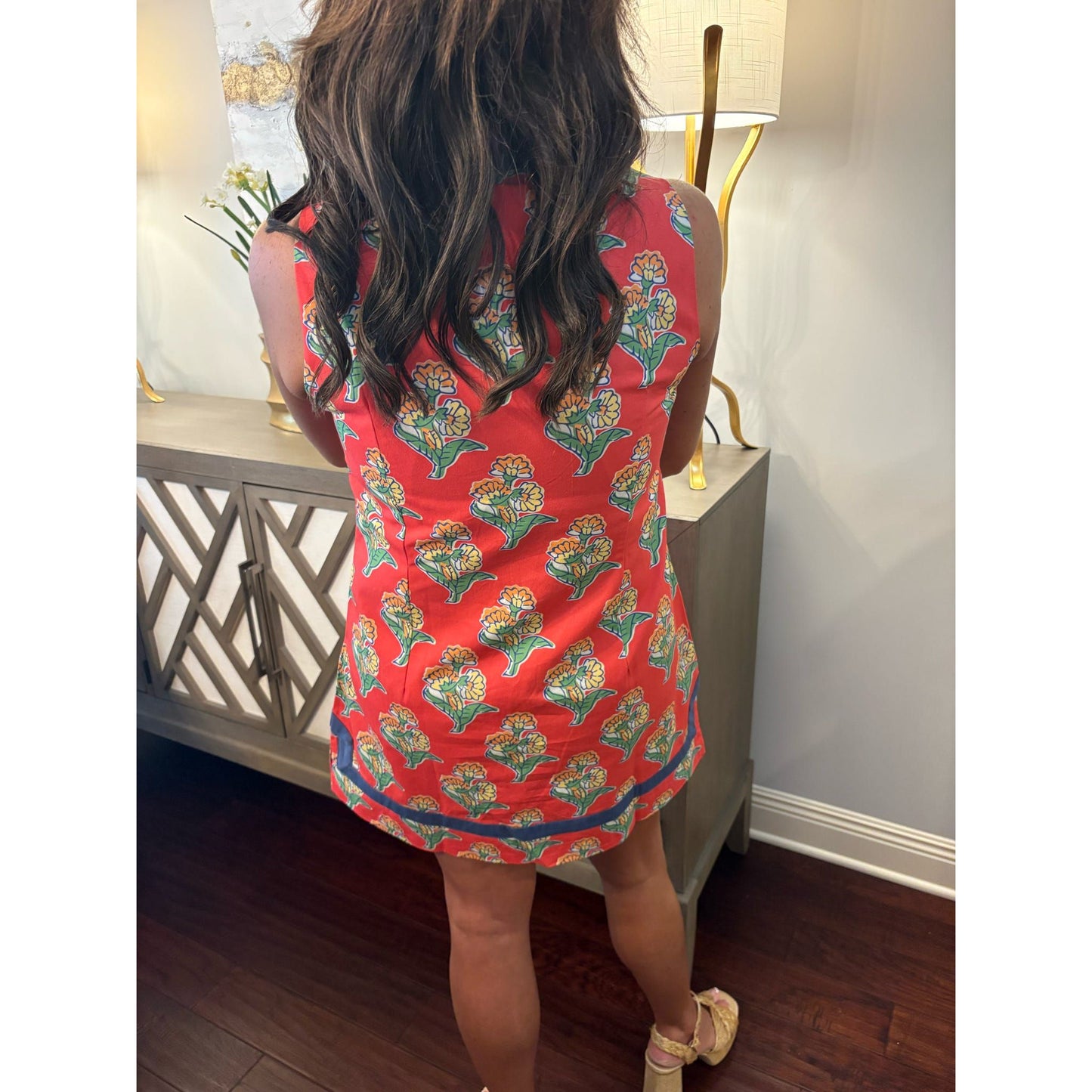 Person wearing a red floral dress in a room with a lamp and decorative items.