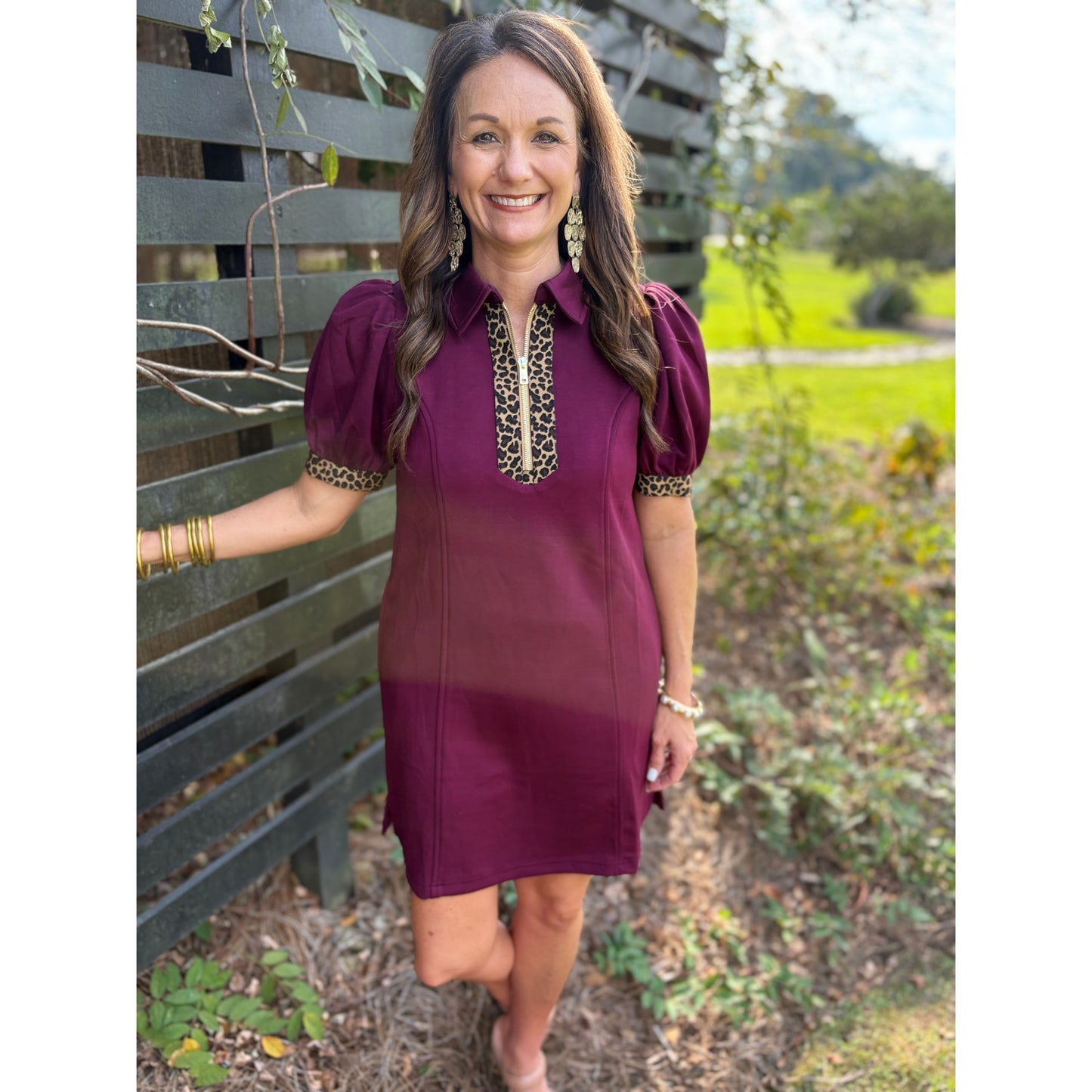 Woman wearing a burgundy dress with gold embellishments standing outdoors.