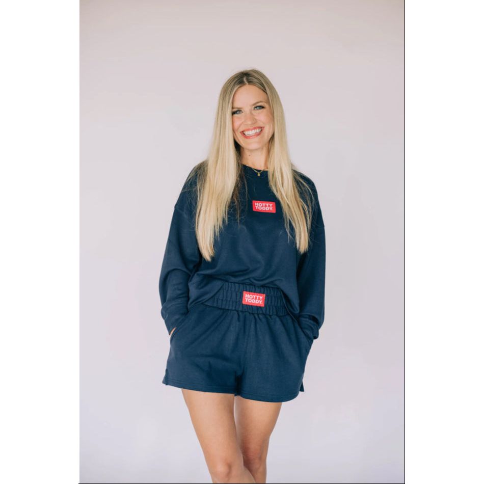 Woman wearing a navy blue outfit with red labels against a plain background