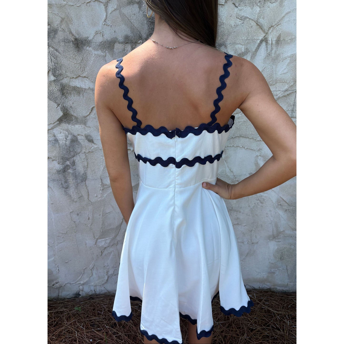 White dress with navy blue trim worn by a person against a stone wall.