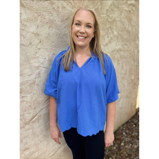 Woman wearing a blue shirt standing against a stone wall.