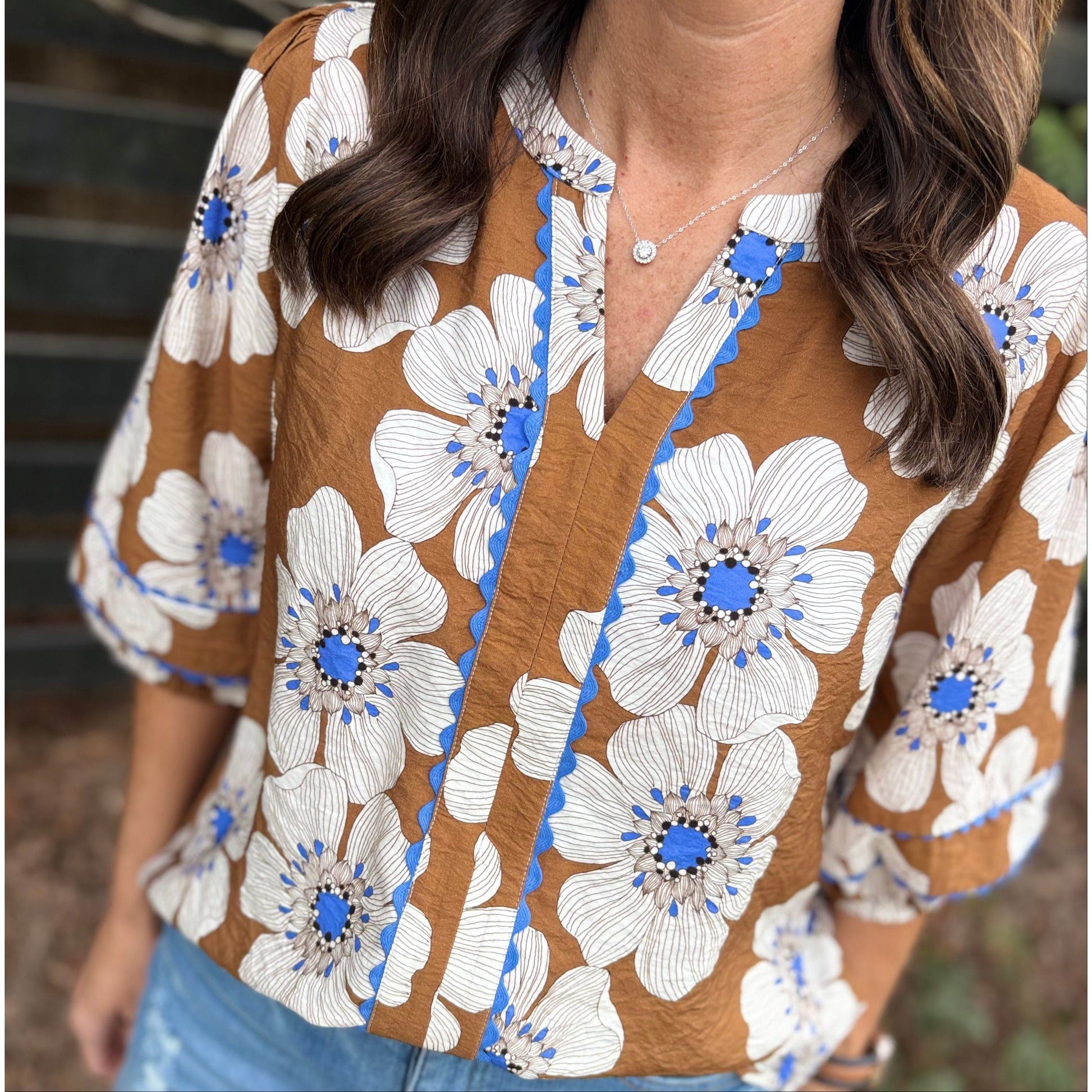 Woman wearing a brown floral blouse with blue centers, standing outdoors.