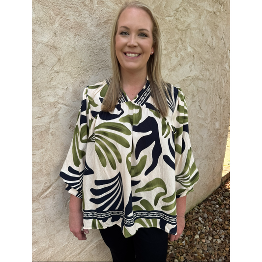 Woman wearing a patterned blouse standing against a stone wall.