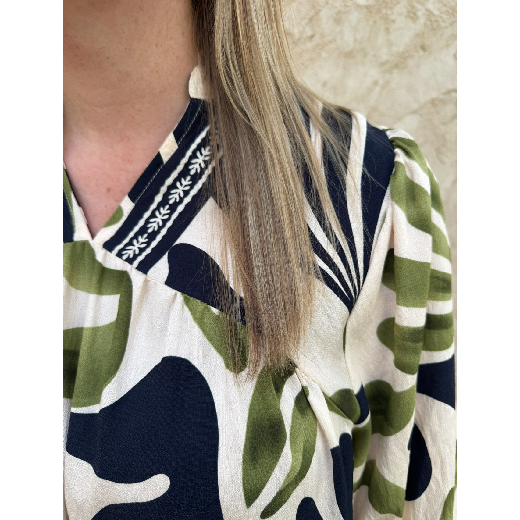 Person wearing a patterned shirt with green, white, and navy colors against a beige wall.
