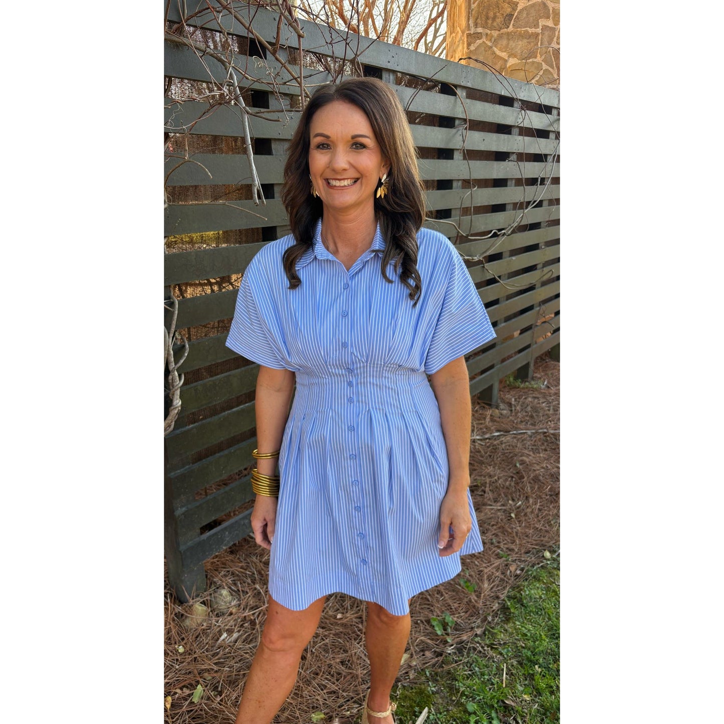 Woman in a blue dress standing in front of a wooden fence.