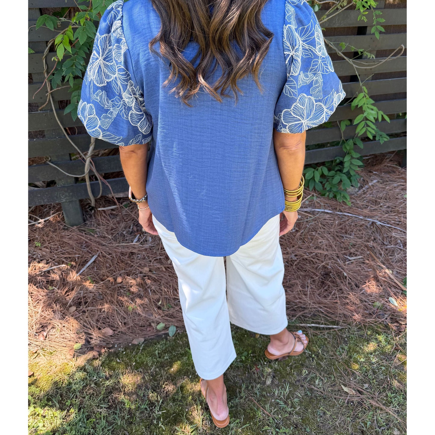 Person wearing a blue vest and white pants bending over in a garden setting.