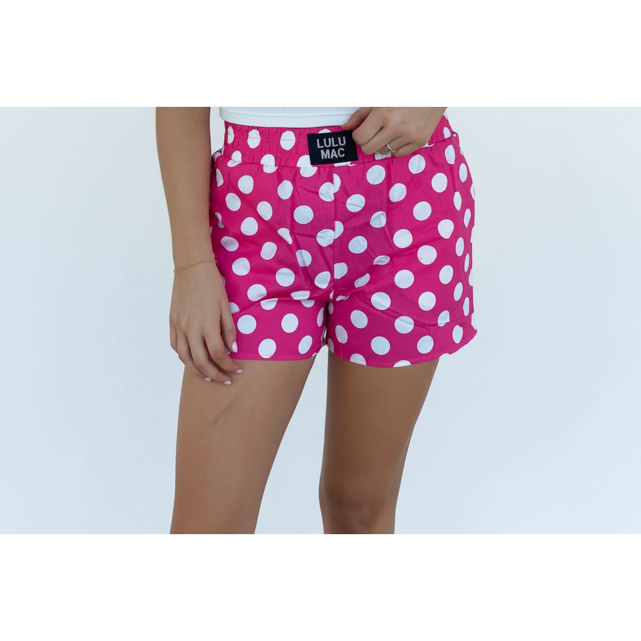 Person wearing pink polka dot shorts with Lulu Mac label against a white wall.